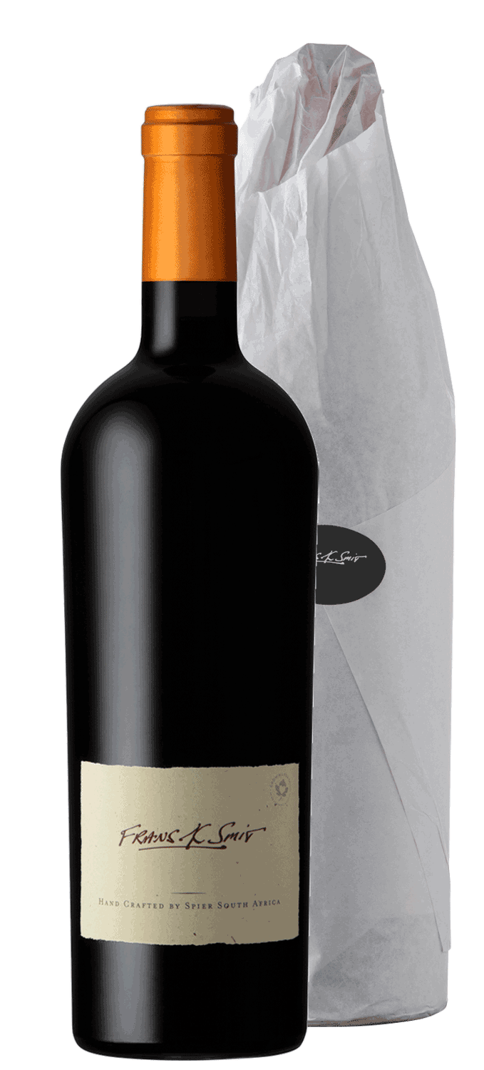 Eine dunkle Weinflasche mit einem kupferfarbenen Foliendach und einem cremefarbenen Etikett mit der Aufschrift Frans K. Smit, Hand Crafted by Spier South Africa, steht neben einer in weißes Seidenpapier eingewickelten Flasche mit einem schwarzen ovalen A