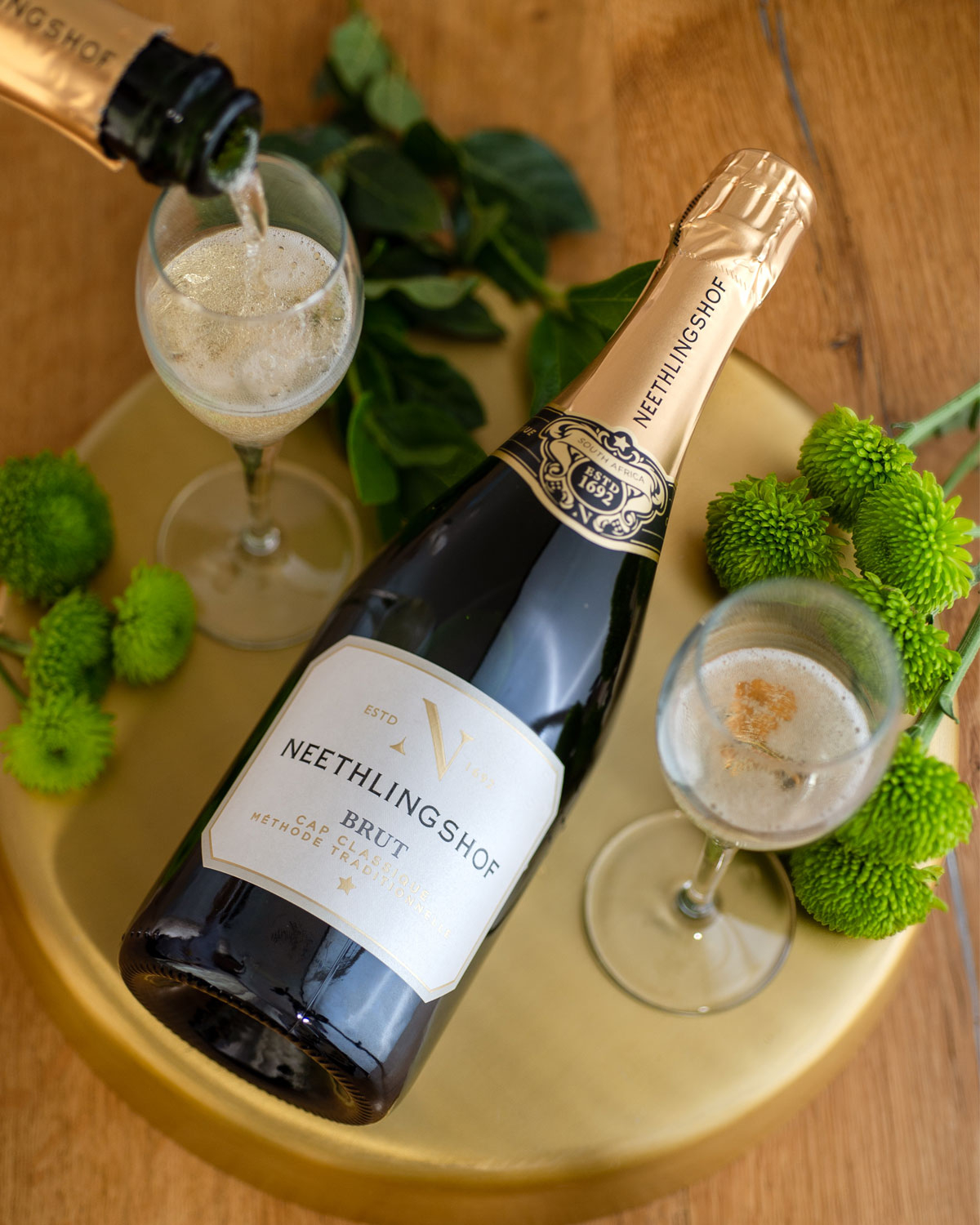 Eine grüne Flasche Neethlingshof Brut Sekt mit einem Hals aus Goldfolie, einem verschnörkelten schwarz-goldenen Etikett oben und einem weiß-goldenen Hauptetikett auf der Vorderseite, auf dem der Markenname und weitere Angaben stehen.