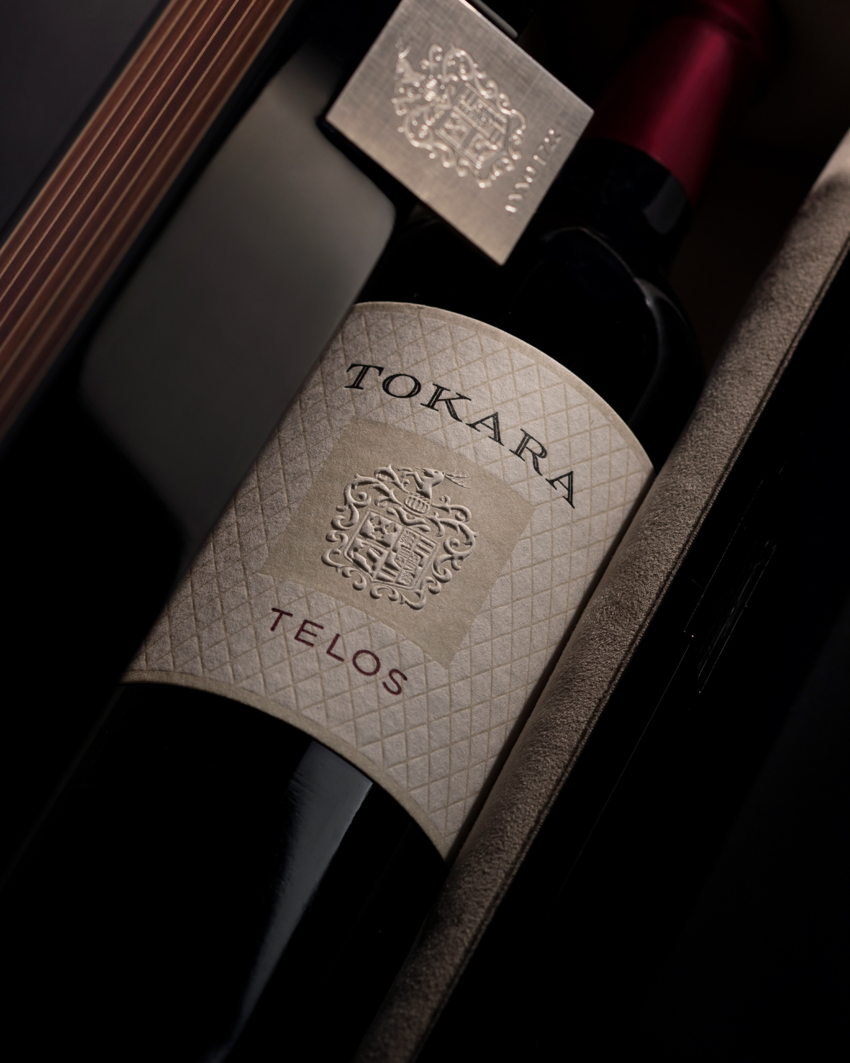 Nahaufnahme einer Tokara Telos Weinflasche in einer eleganten Schachtel mit einem cremefarbenen Etikett mit Wappen und goldenen Akzenten, das teilweise vom Schachteldeckel verdeckt wird.