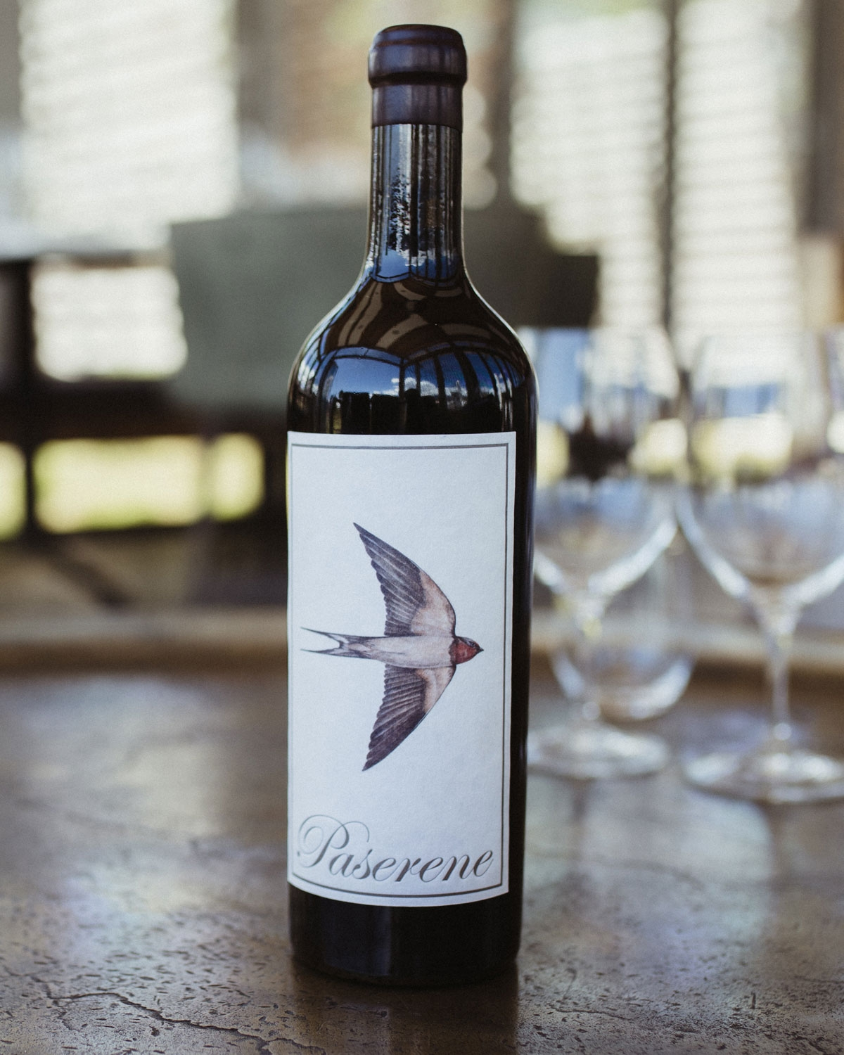 Eine dunkle Weinflasche mit einem burgunderroten Foliendeckel und einem Etikett mit der Abbildung einer fliegenden Schwalbe und dem Wort Pasarene in eleganter Schrift am unteren Rand.