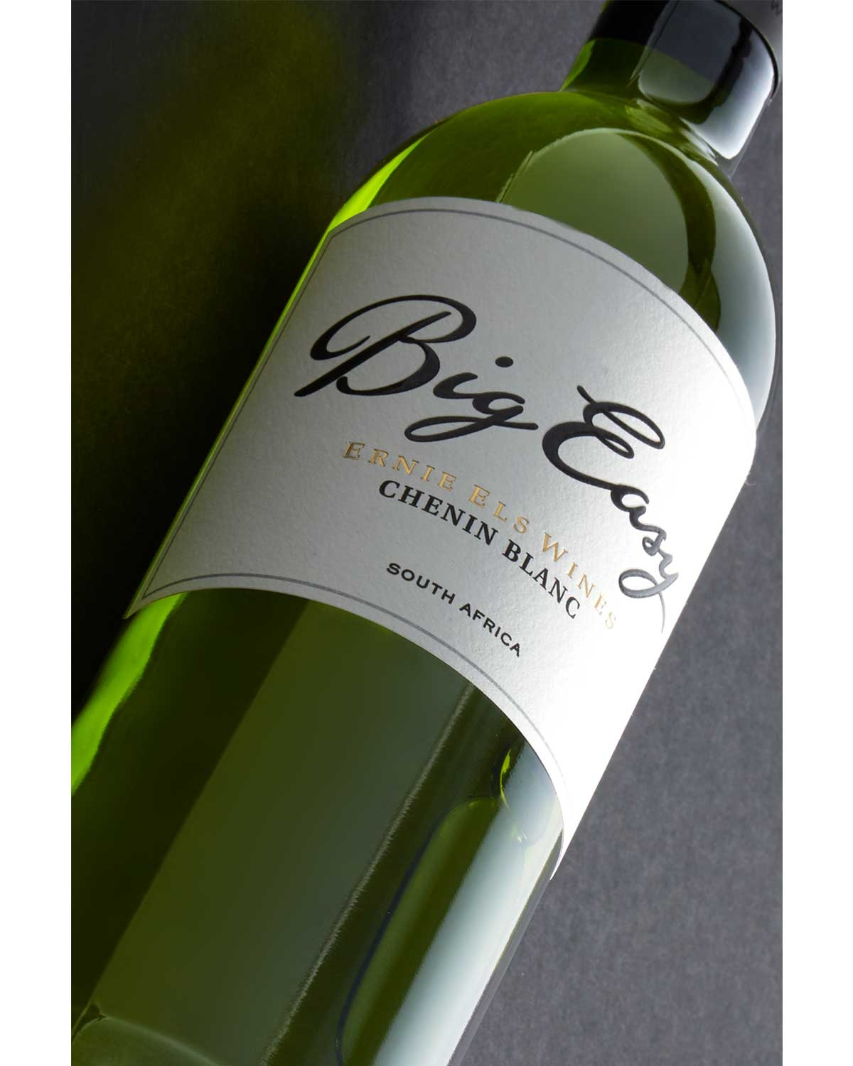 Eine Nahaufnahme einer grünen Weinflasche mit der Aufschrift Big Easy Ernie Els Wines Chenin Blanc, Südafrika, vor einem dunklen Hintergrund. Die Flasche ist diagonal gekippt, so dass das Etikett deutlich zu sehen ist.
