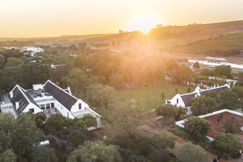 Luftaufnahme des Weinguts Spier bei Sonnenuntergang mit historischen Gebäuden und umliegenden Weinbergen