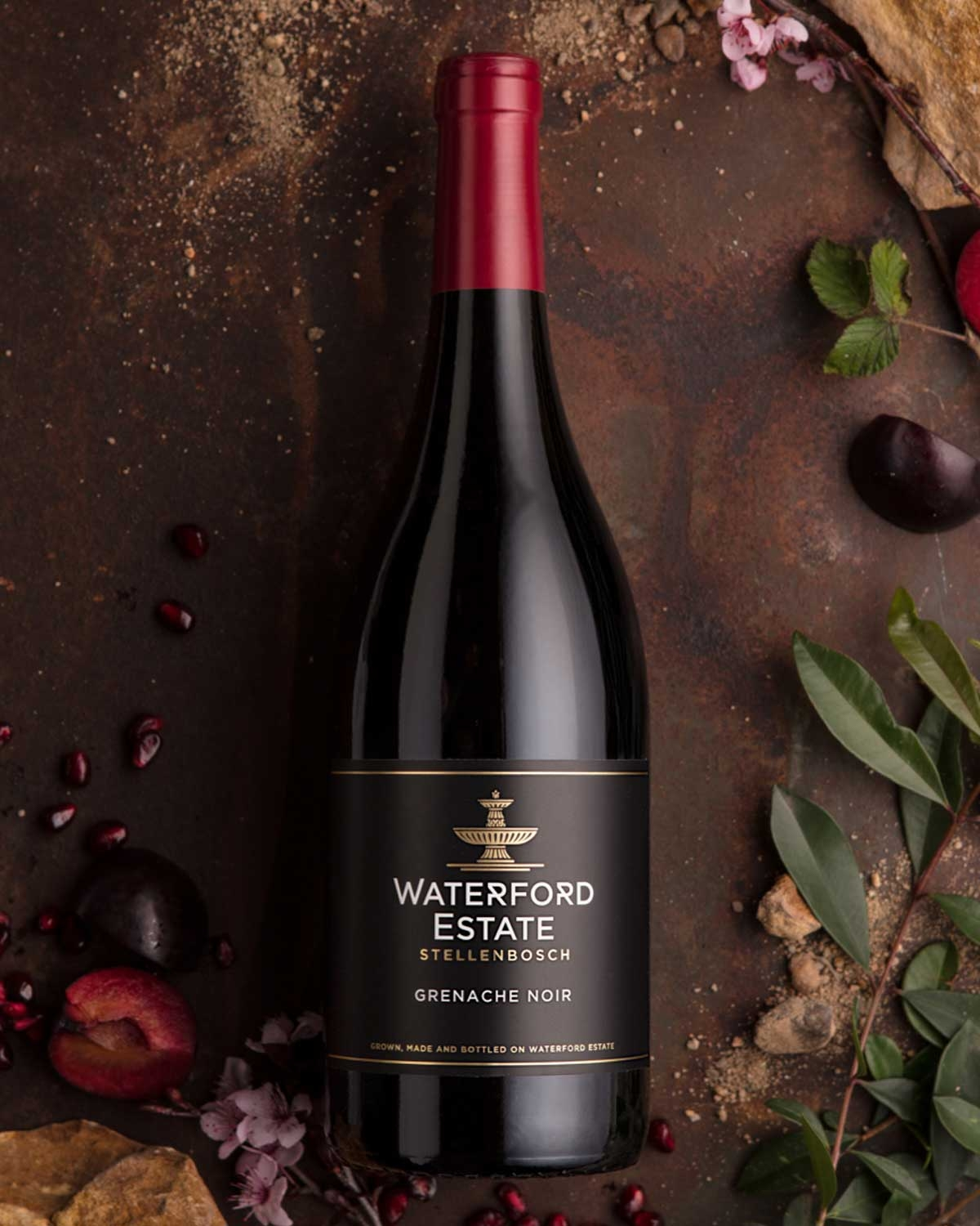 Eine Flasche Waterford Estate Stellenbosch Grenache Wein mit rotem Folienverschluss und schwarzem Etikett mit goldener und weißer Schrift und goldenem Emblem.