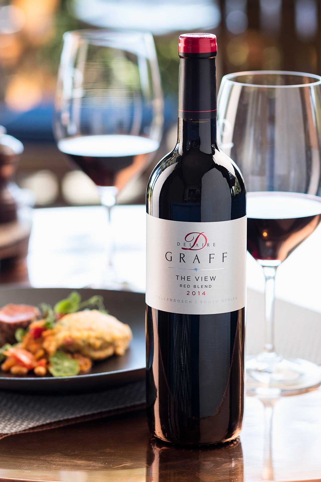 Flasche Delaire Graff Rotwein mit gefülltem Weinglas und Gourmet-Essen im Hintergrund