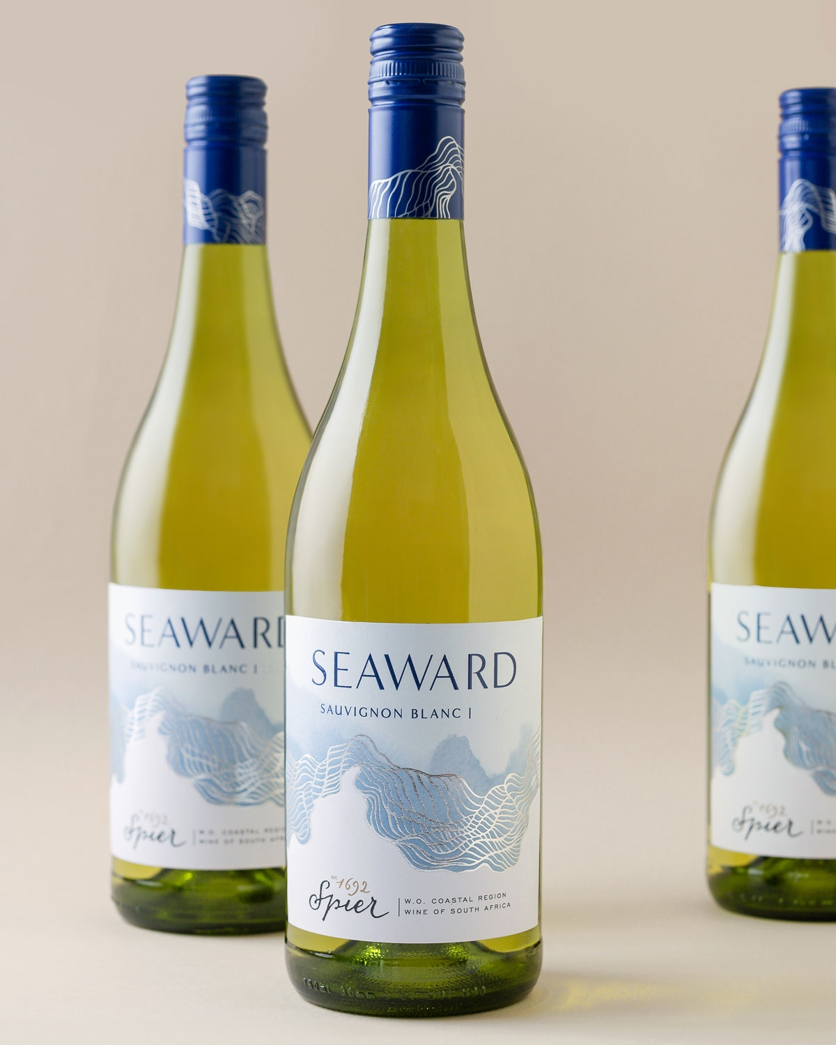 Eine Flasche Seaward Sauvignon Blanc mit einem blauen Schraubverschluss und einem Etikett mit wellenförmigen Motiven, dem Markennamen "Seaward" und einem Text, der angibt, dass der Wein aus Spier, Südafrika, stammt.