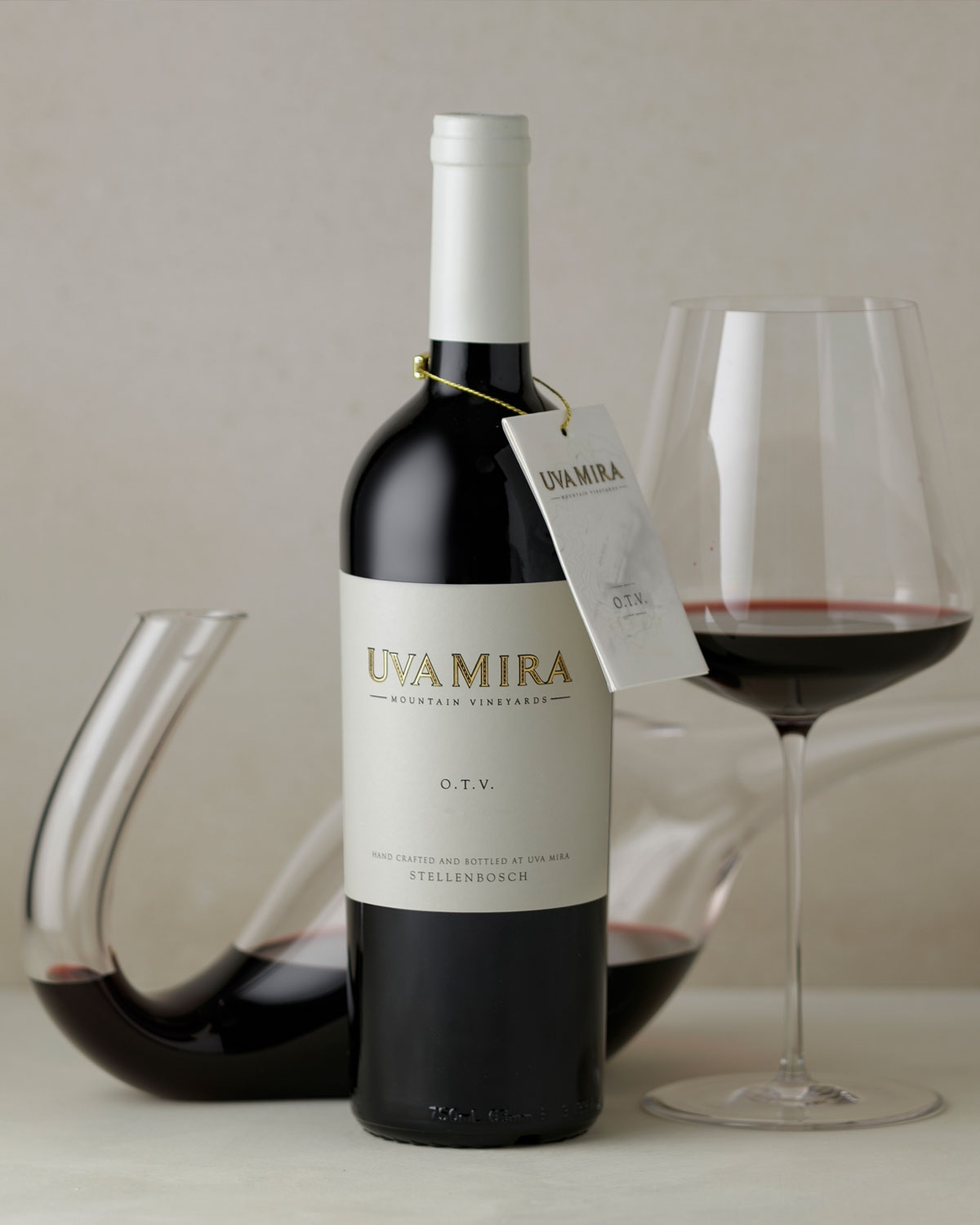 Eine Flasche Uva Mira Mountain Vineyards O.T.V. Rotwein mit einem cremefarbenen Etikett und einem um den Hals hängenden Anhänger. Auf dem Etikett steht, dass er in Stellenbosch handgefertigt und abgefüllt wurde.