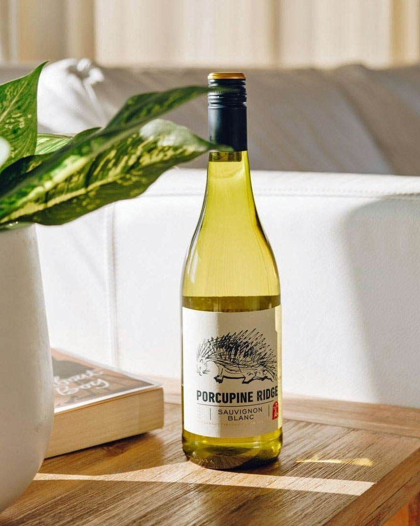 Eine grüne Flasche Porcupine Ridge Sauvignon Blanc mit einem weißen Etikett, auf dem ein schwarzes Stachelschwein abgebildet ist, und einem Text, der den Namen und die Herkunft des Weins aus Südafrika beschreibt.