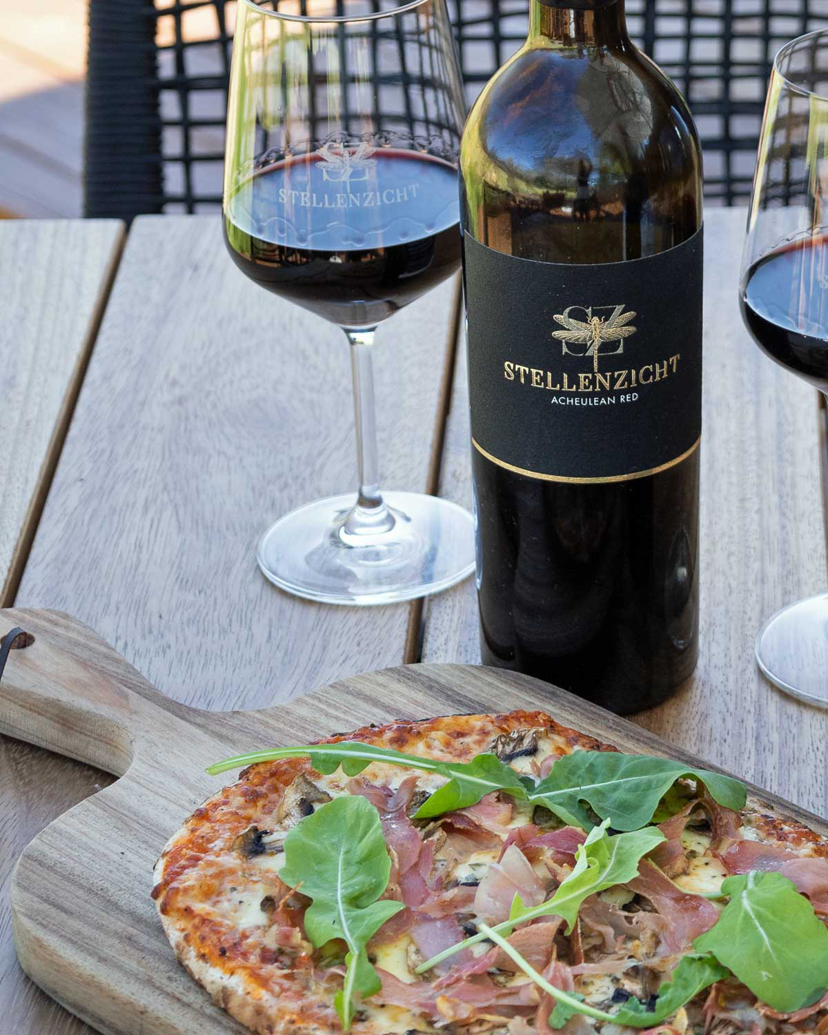 Eine dunkle Weinflasche mit einem schwarz-goldenen Etikett, das eine Libelle und den Text Stellenzicht Acheulean Red zeigt. Der Deckel der Flasche ist mit einer Goldfolie überzogen.