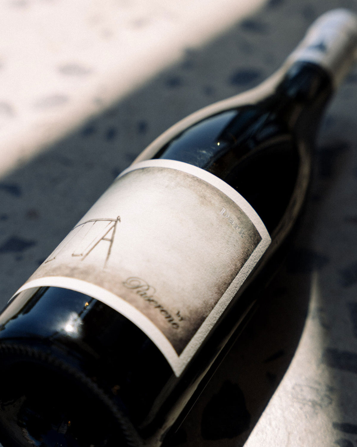 Eine dunkle Weinflasche mit einem silbernen Folienverschluss und einem Etikett, das eine Schwarz-Weiß-Abbildung einer leeren Schaukel vor einem nebligen Hintergrund zeigt. Auf dem Etikett steht "Dark" und "by Pasarene".