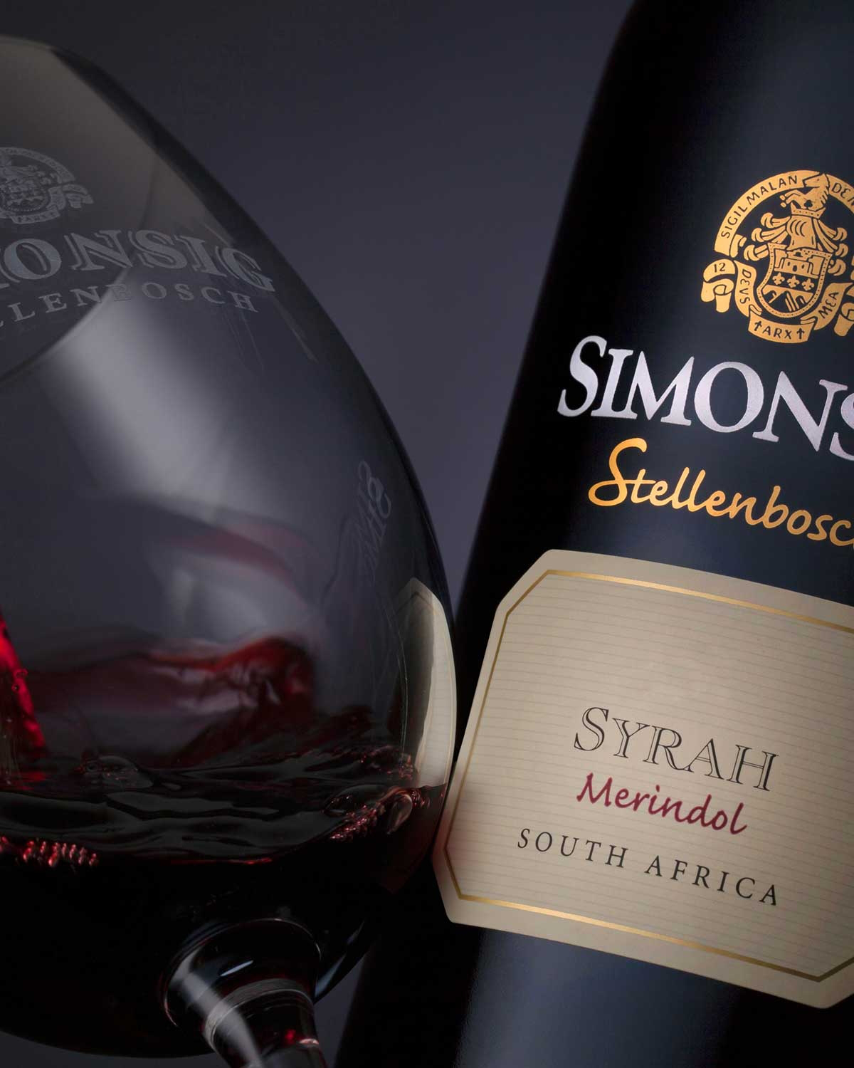 Eine dunkle Weinflasche mit der Aufschrift Simonsig Stellenbosch Syrah Merindol South Africa, mit goldenem Text und einem goldenen Emblem auf der Vorderseite.