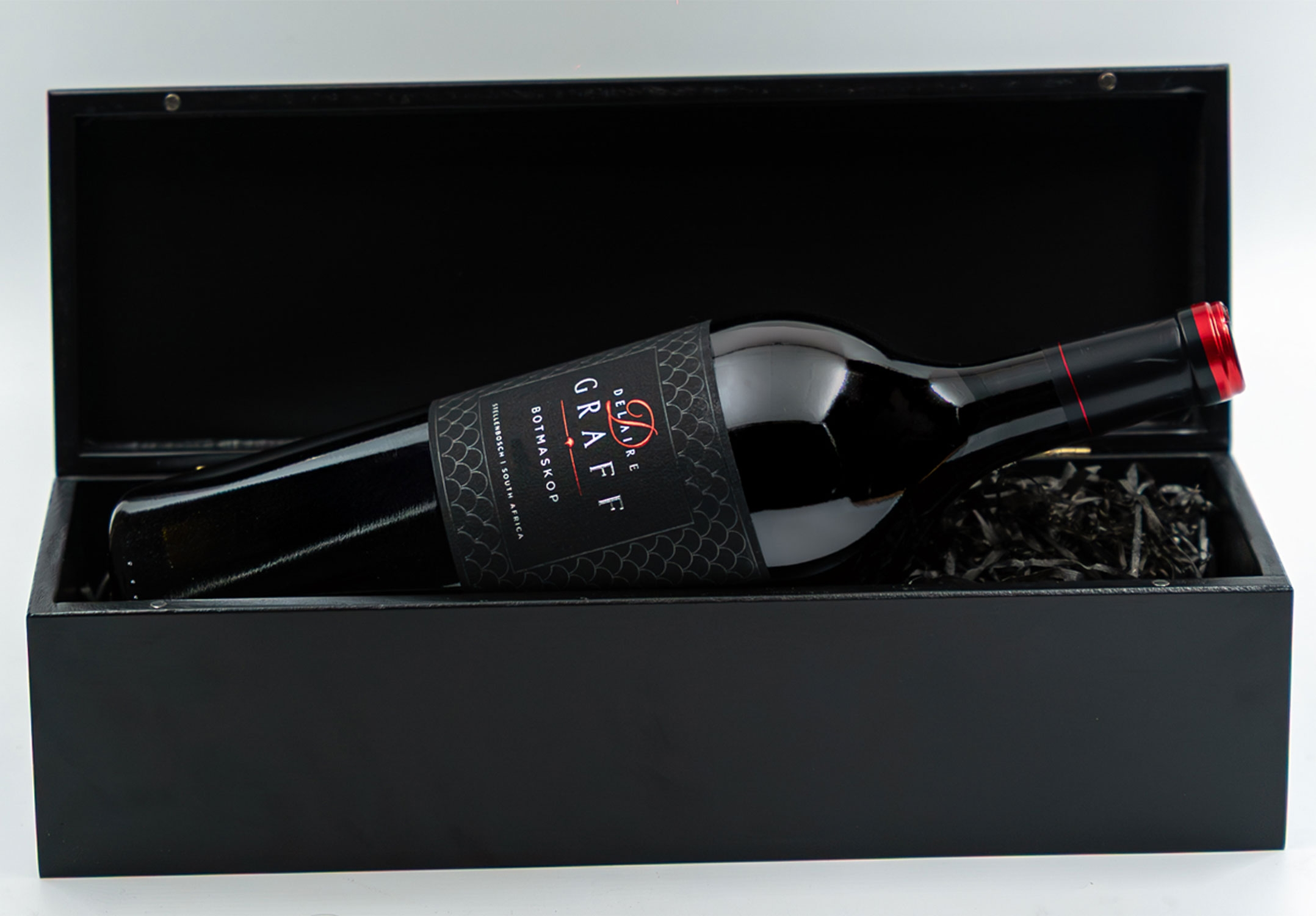Eine große dunkle Glasflasche Delaire Graff Botmaskop Rotwein mit einem schwarzen und roten Etikett, und eine rote Folie Kapsel über den Korken. Das Etikett zeigt an, dass es aus Stellenbosch, Südafrika ist.