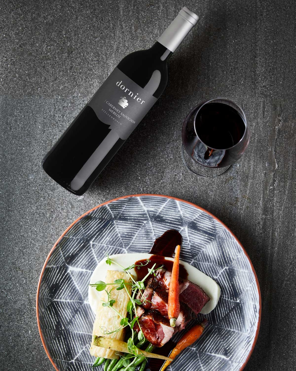 Eine Flasche Dornier Rotwein mit einem silbernen Verschluss und einem dunkelgrauen Etikett, auf dem Cabernet Sauvignon Merlot, Stellenbosch, Südafrika, steht.