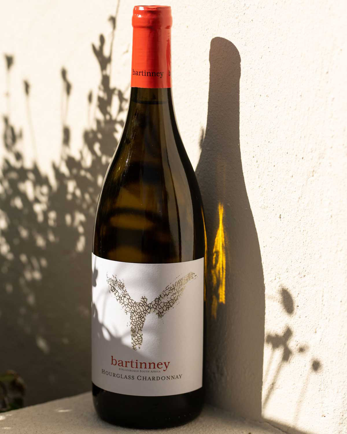 Eine Flasche Bartinney Hourglass Chardonnay mit einem roten Verschluss. Das weiße Etikett zeigt den Namen Bartinney, eine stilisierte Weinrebe und den Text Hourglass Chardonnay.