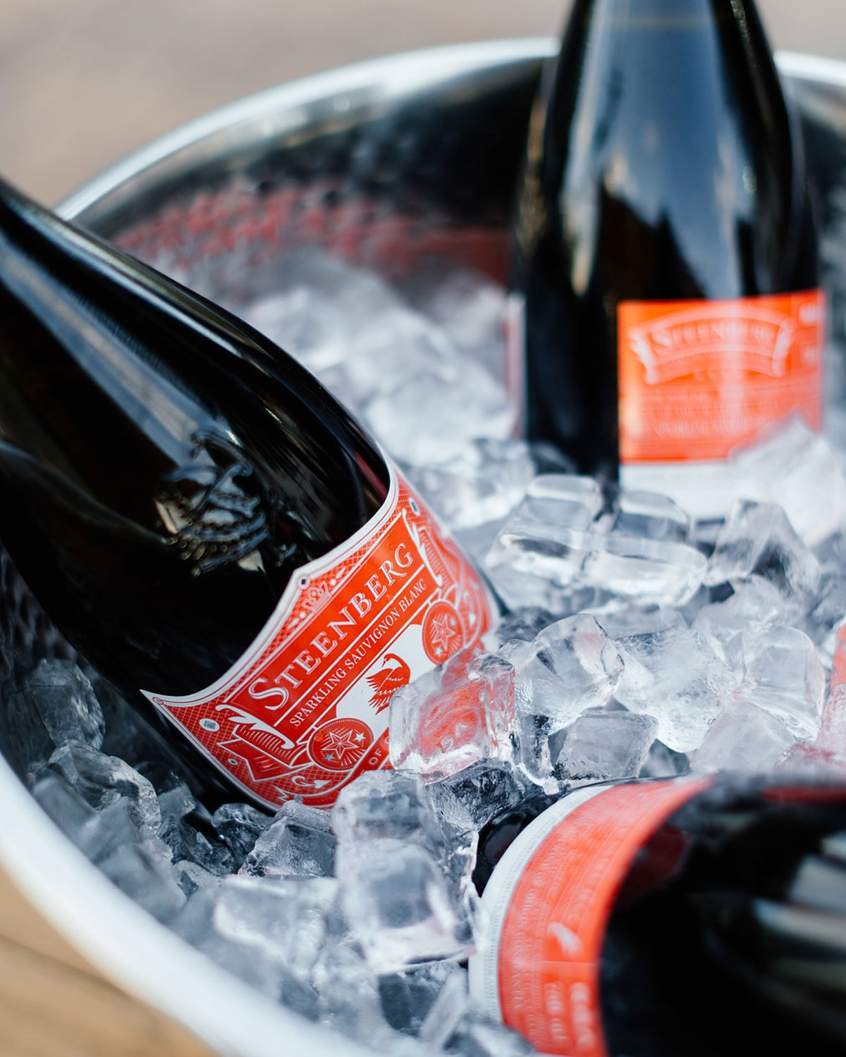 Nahaufnahme von drei dunklen Glasflaschen mit der Aufschrift Steenberg in einem mit Eiswürfeln gefüllten Metalleimer, der die Flaschen kühl hält.