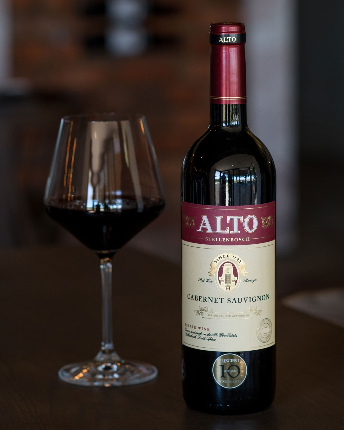 Eine Flasche Alto Stellenbosch Cabernet Sauvignon mit einem rot-goldenen Etikett mit dem Alto-Logo, einer Illustration des Weinguts und einem Text, der den Ursprung des Weins in Südafrika beschreibt.