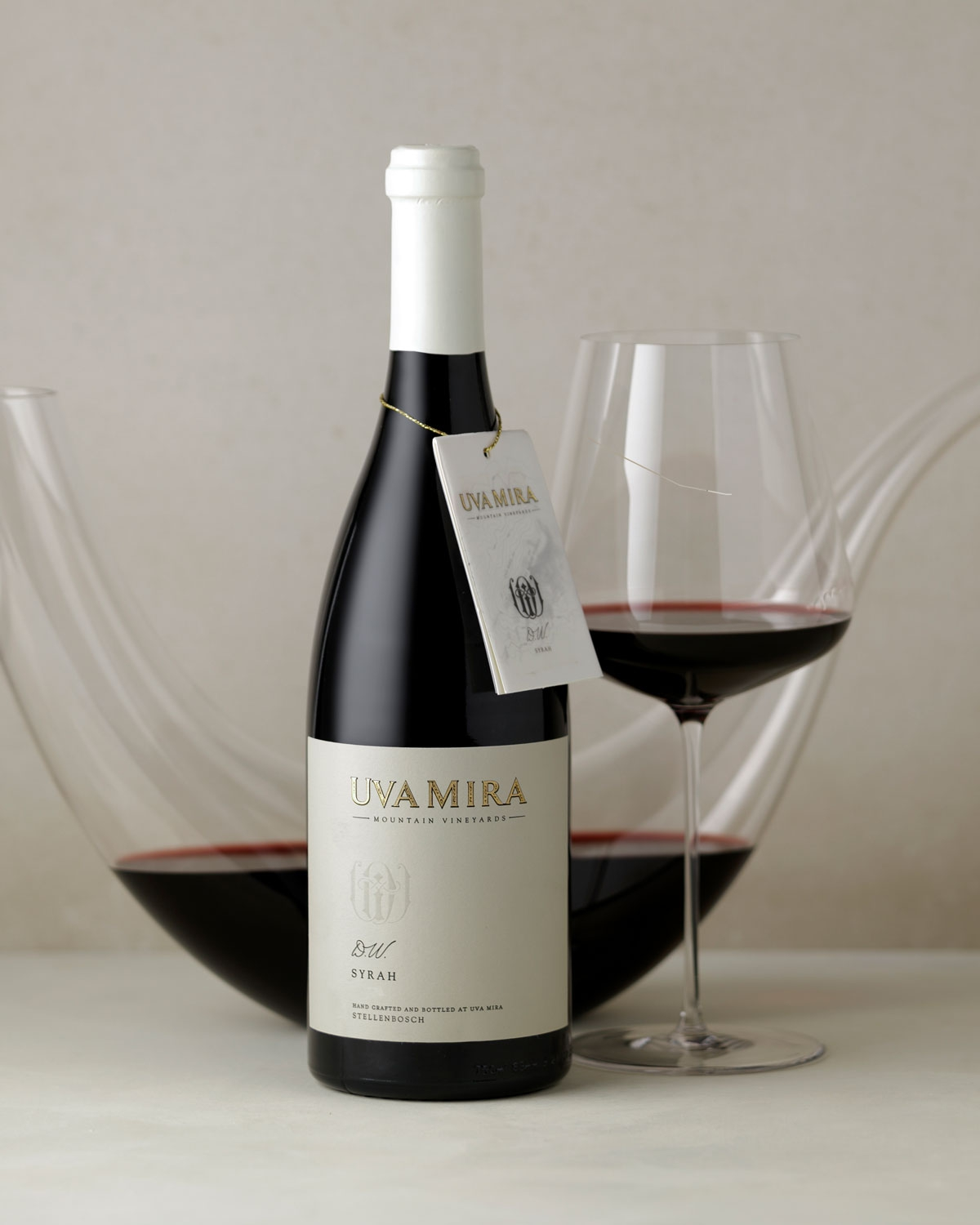 Eine Flasche Uva Mira Mountain Vineyards Syrah Wein mit einem cremefarbenen Etikett und einem passenden Anhänger, der um den Hals hängt. Die Flasche hat ein dunkles Glas und eine helle Folie auf der Oberseite.