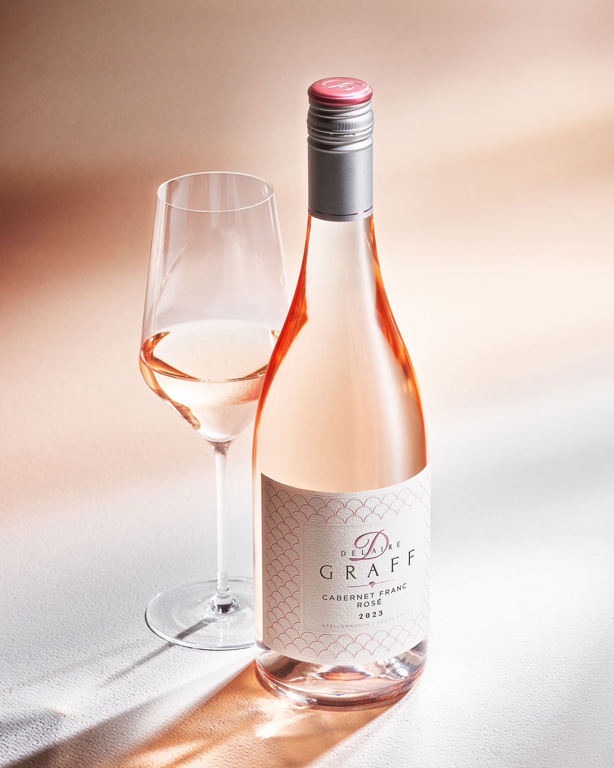 Eine Flasche Delaire Graff Cabernet Franc Rosé mit zartrosa Farbton, silbernem Schraubverschluss und weißem Etikett mit zarten rosa Mustern und elegantem Text.