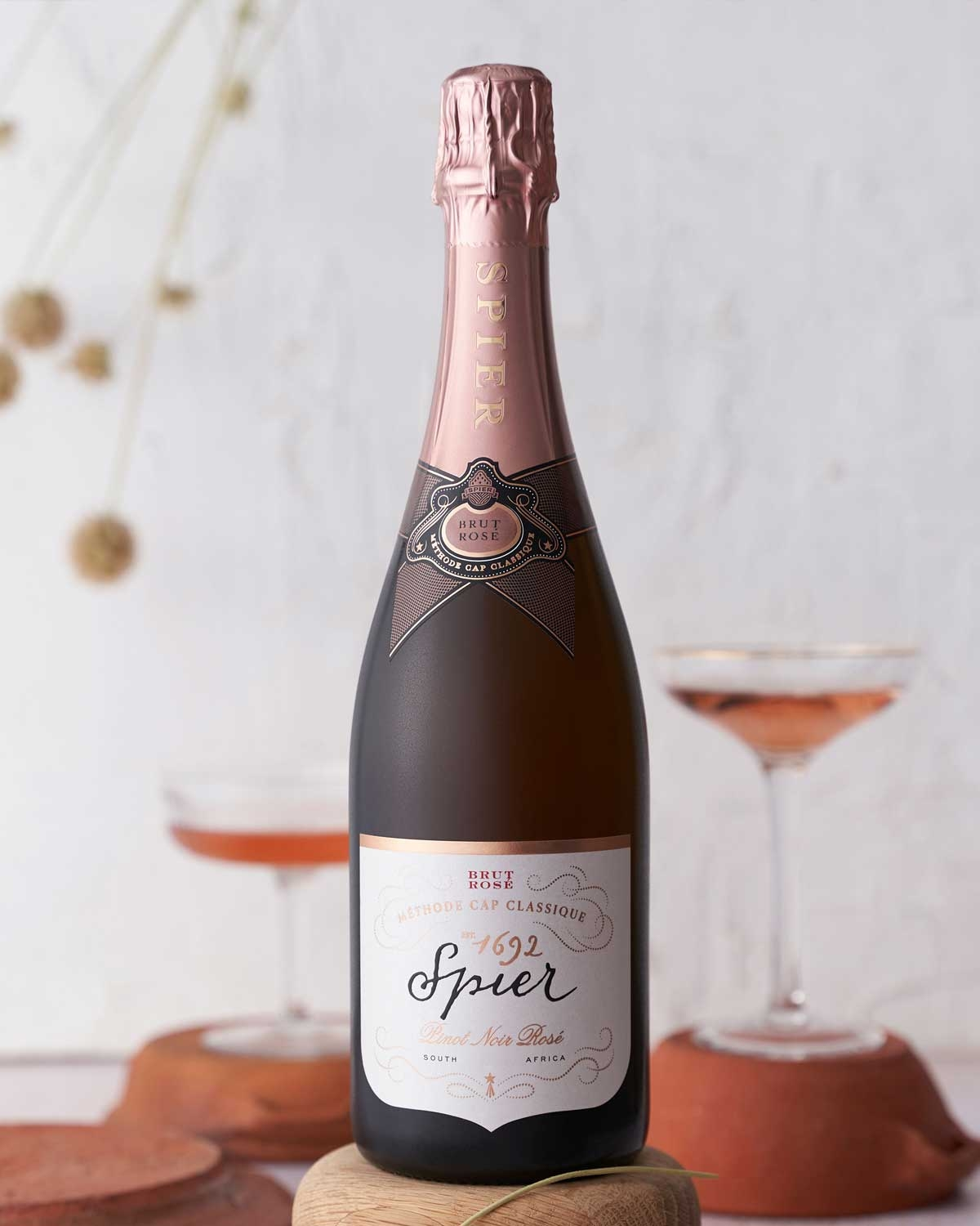 Eine Flasche Spier Pinot Noir Rosé Méthode Cap Classique Sekt mit einem rosa Folienverschluss und einem eleganten weiß-rosa Etikett mit goldenen Akzenten.