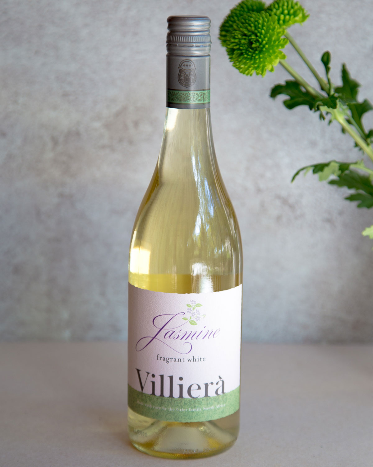 Eine Flasche Villiera Jasmin duftenden Weißwein, mit einer blassgrünen Kappe und einem cremefarbenen Etikett mit lila und grünen Text und floralen Akzenten. Der Wein im Inneren ist hellgelb in der Farbe.