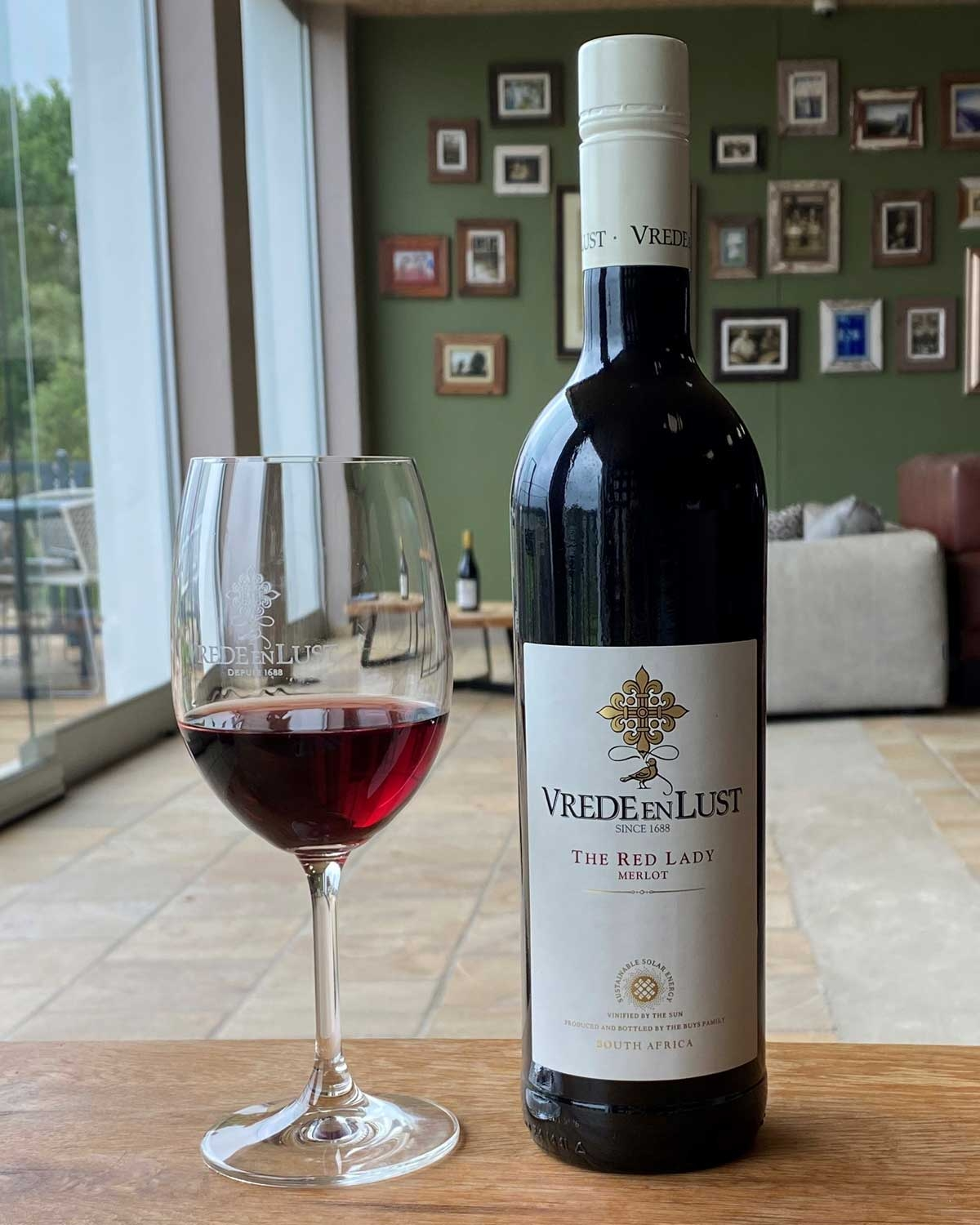 Eine Flasche Vrede en Lust The Red Lady Merlot Wein aus Südafrika mit einem weißen Etikett mit goldenem und rotem Text und einem dekorativen Emblem in der Mitte.
