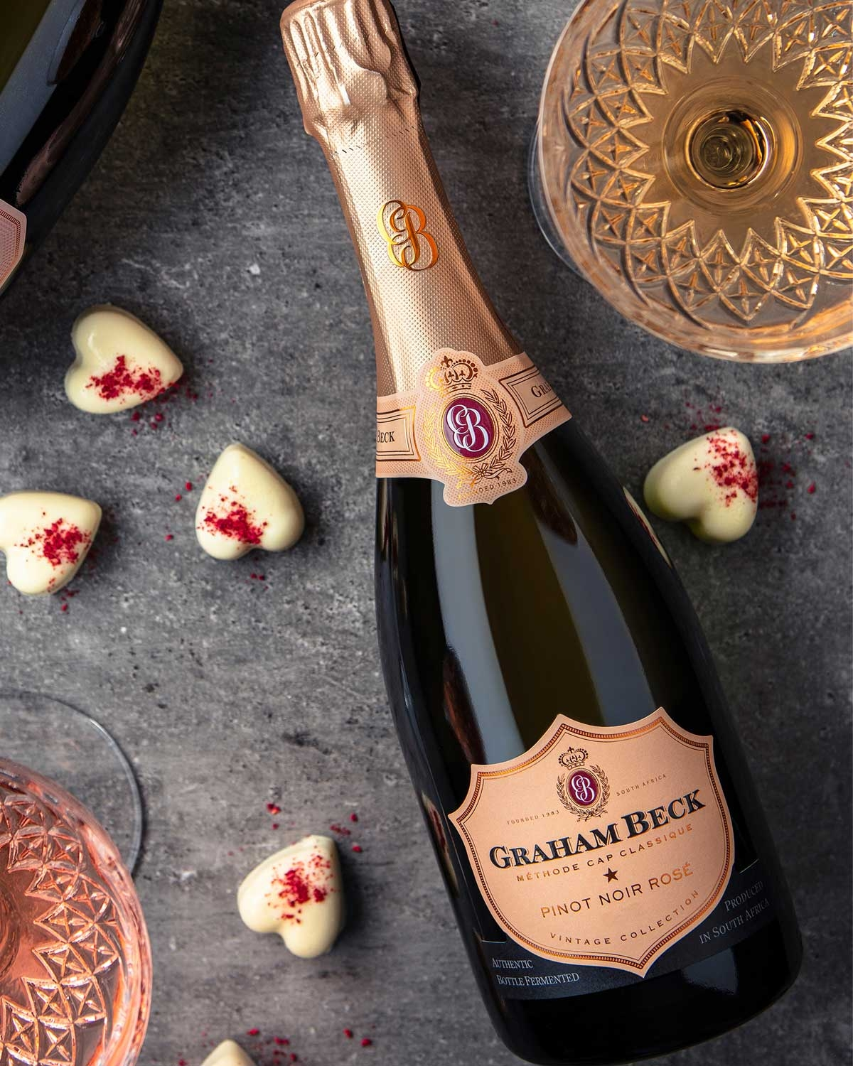 Eine Flasche Graham Beck Pinot Noir Rosé Sekt mit einem Hals aus Goldfolie und einem pfirsichfarbenen Etikett mit elegantem Branding und dem Hinweis, dass er in Südafrika hergestellt wurde.