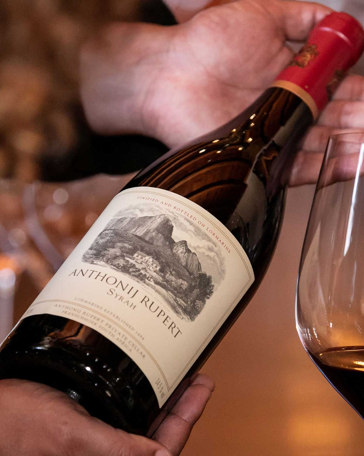 Eine Weinflasche aus dunklem Glas mit kastanienbraunem und goldenem Verschluss, mit einem braunen Etikett mit der Aufschrift Anthonij Rupert Syrah und einer Illustration von Bergen, aus LOrmarins Private Cellar in Franschhoek, Südafrika.