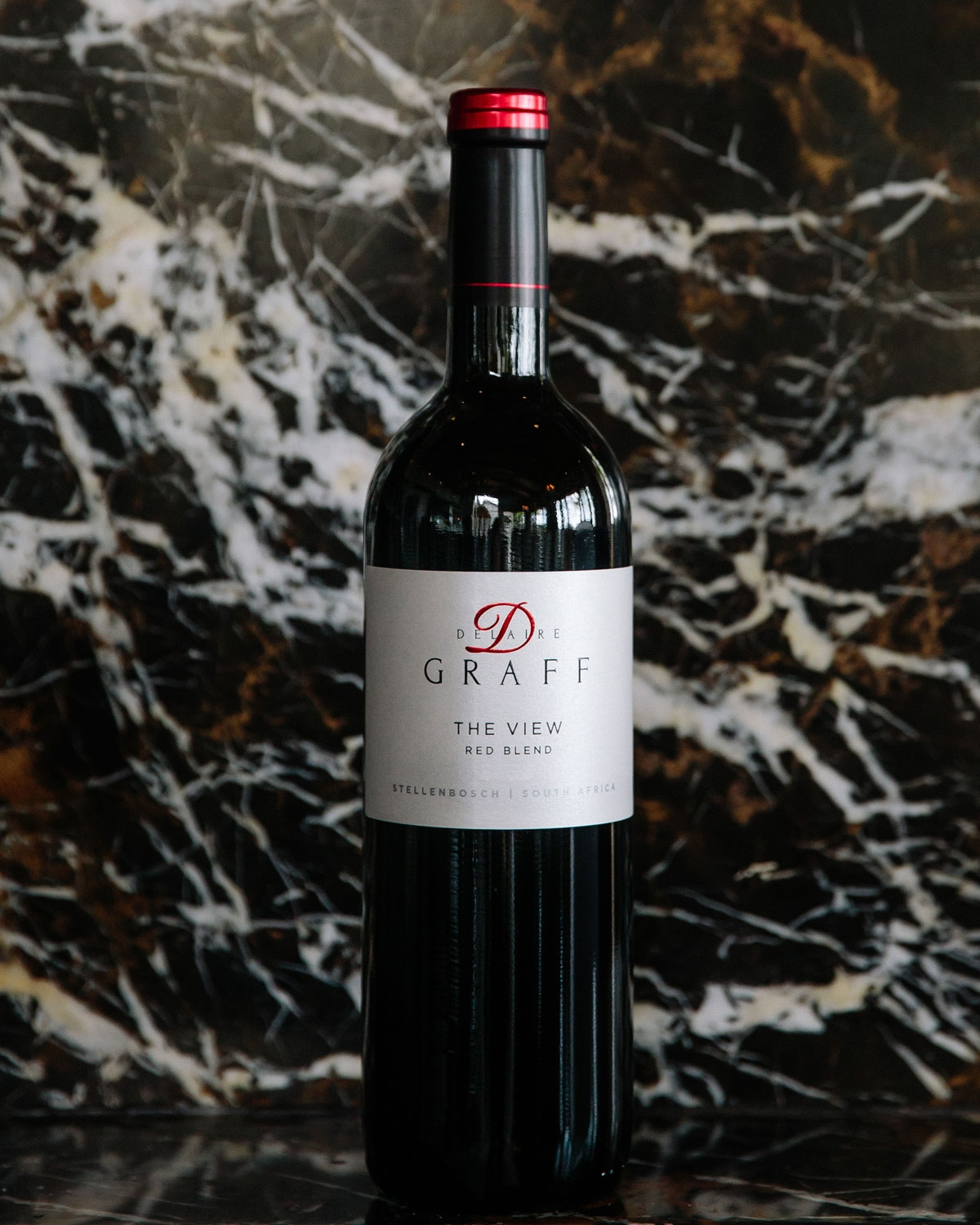 Eine Flasche des Rotweins Delaire Graff The View steht aufrecht vor einem dunklen Marmorhintergrund mit weißen und goldenen Adern.