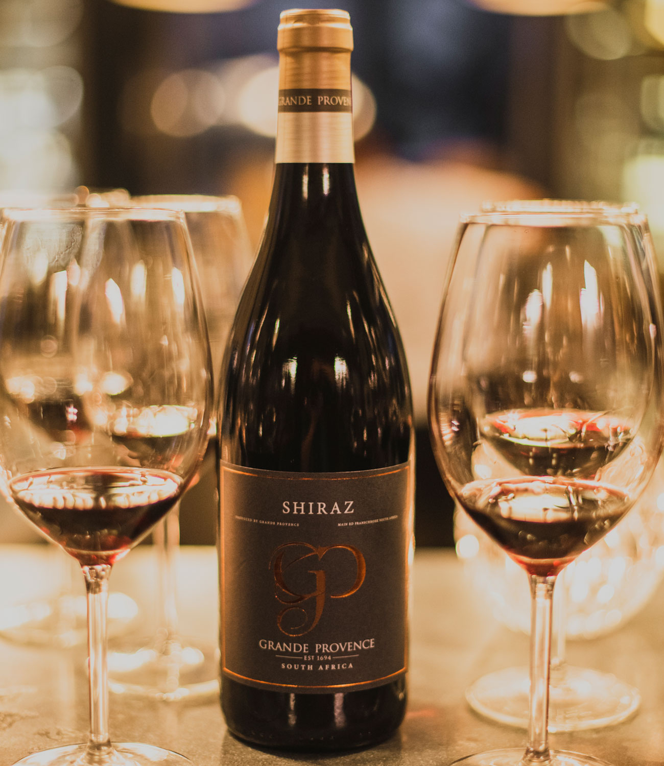 Eine Flasche Grande Provence Shiraz Wein mit schwarzem Etikett, goldener und weißer Schrift und goldenem GP-Logo. Der Hals hat eine braune Folie mit dem Aufdruck GRANDE PROVENCE.