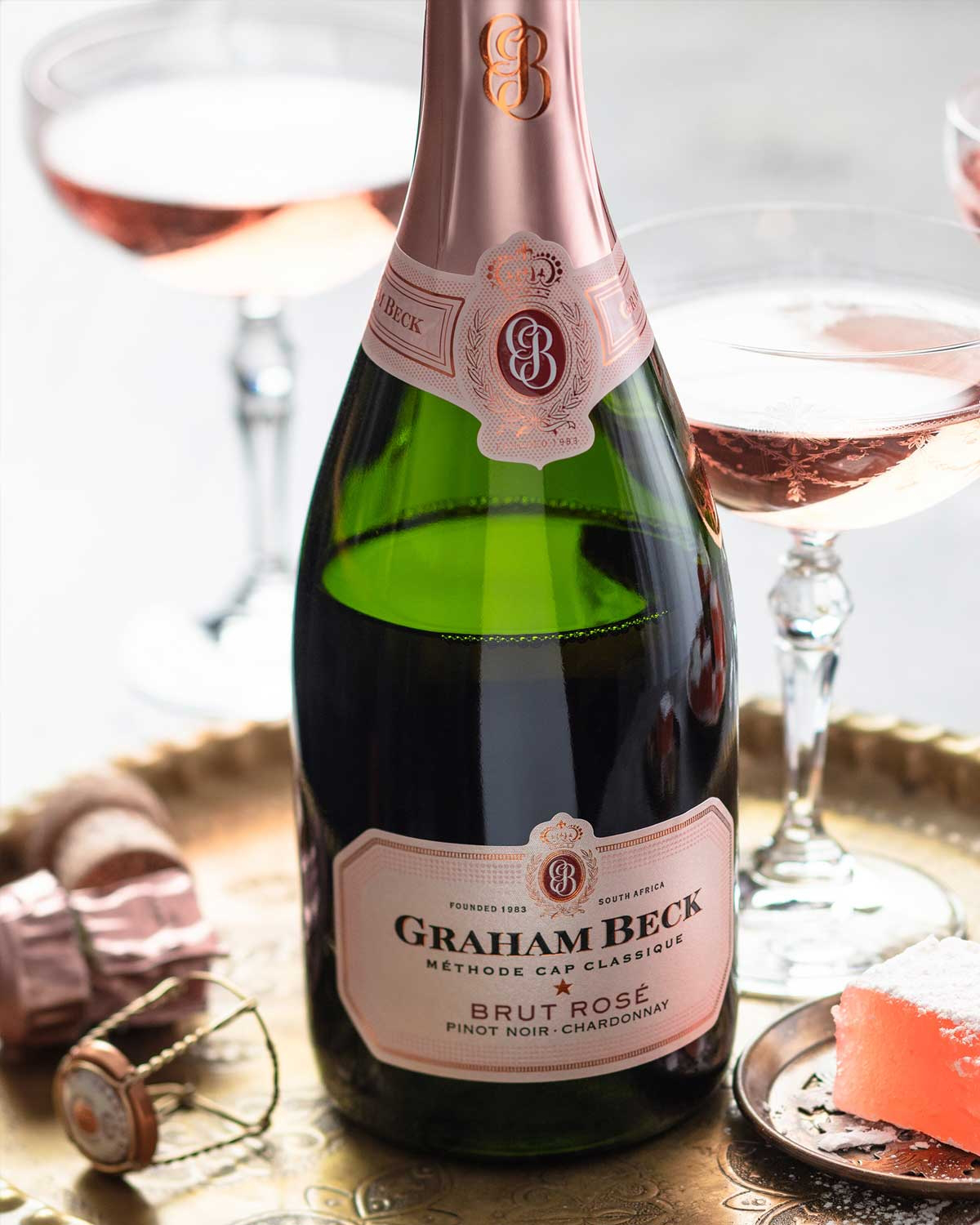 Eine Flasche Graham Beck Brut Rosé Sekt mit einem rosafarbenen Foliendach und einem weiß-rosafarbenen Etikett mit goldenen Akzenten und Branding auf einem schlichten weißen Hintergrund.