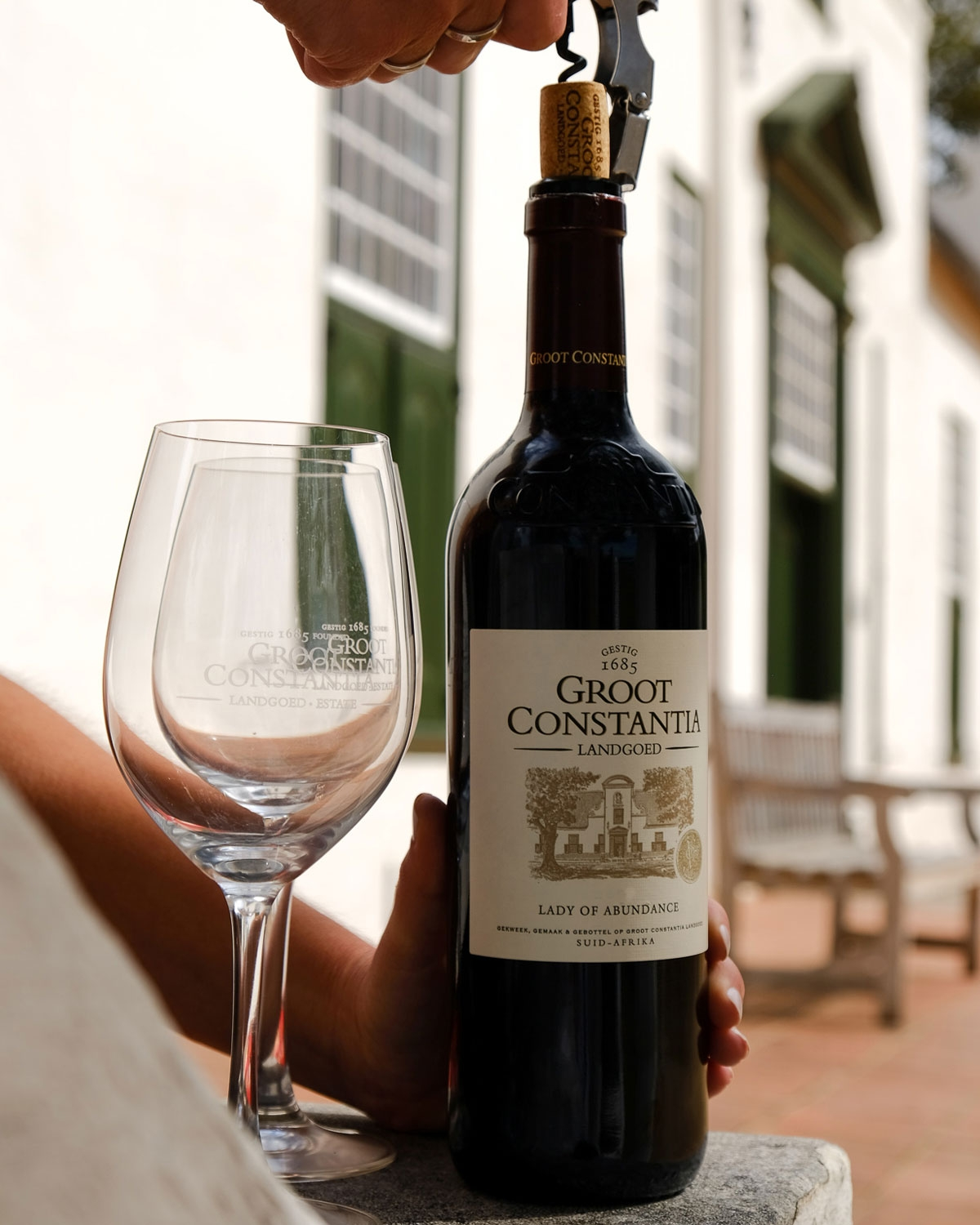 Eine Flasche Groot Constantia Lady of Abundance Rotwein mit einem cremefarbenen Etikett mit einer Skizze eines historischen Gebäudes und dem Emblem einer Goldmedaille sowie einer kastanienbraunen Folie am Hals.