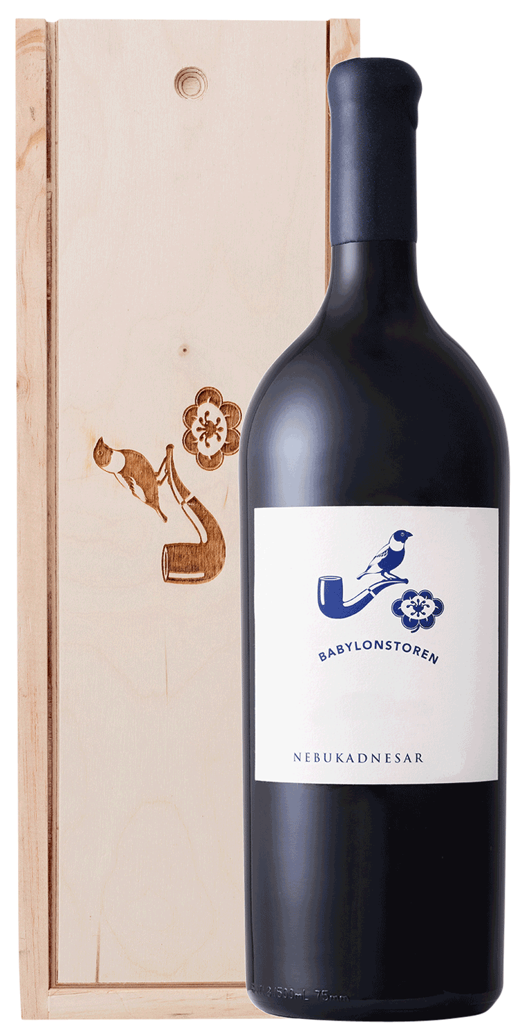 Eine große dunkle Weinflasche mit der Aufschrift Babylonstoren Nebukadnesar steht vor einer Holzkiste mit eingravierten Blumen- und Hornmotiven.
