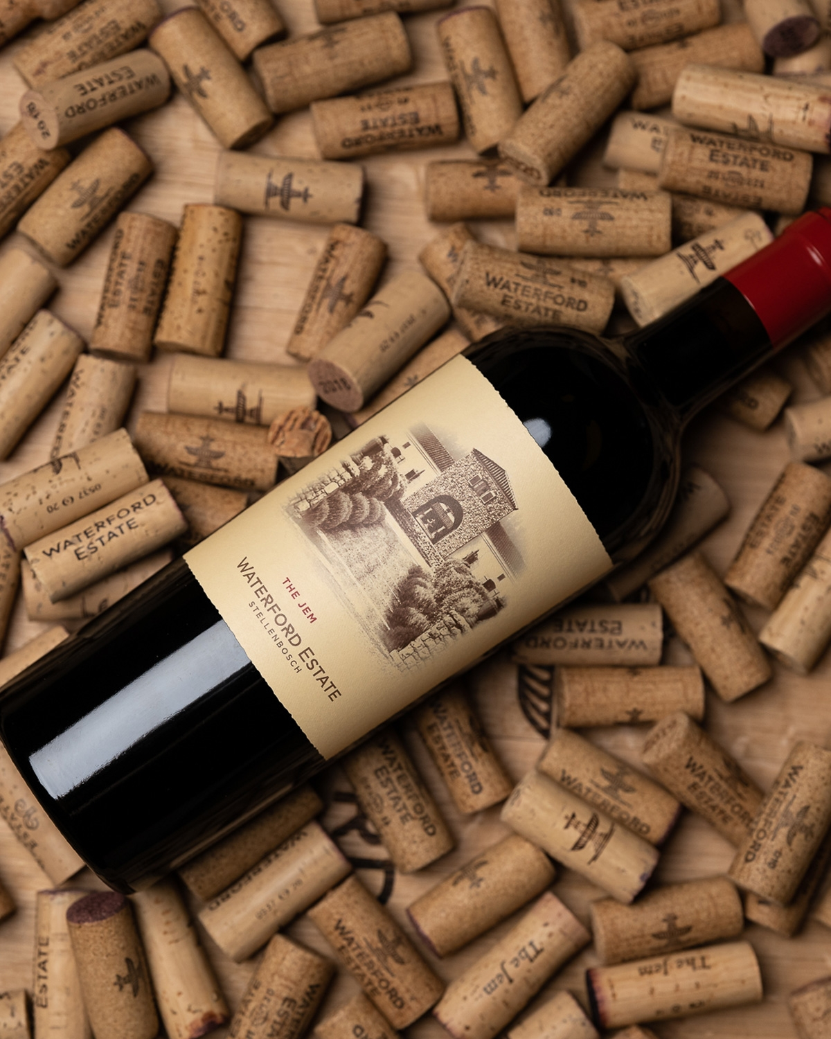 Eine Flasche Waterford Estate Rotwein liegt auf einer Fläche, die mit zahlreichen Weinkorken bedeckt ist, die alle mit dem Waterford Estate-Logo versehen sind.