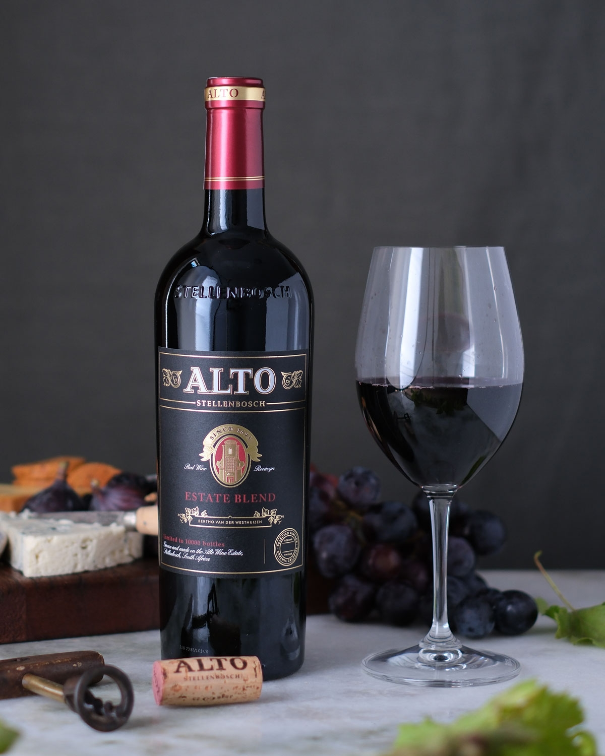 Eine Flasche Alto Estate Blend Rotwein mit einem dunklen Etikett mit goldenen und roten Akzenten, dem Namen ALTO am oberen Rand und einem Text, der angibt, dass er aus Stellenbosch, Südafrika, stammt.