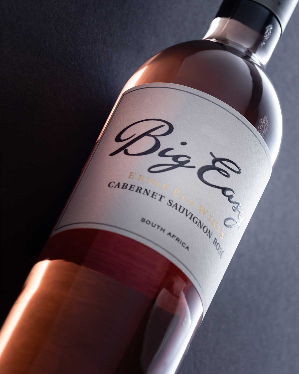 Eine Flasche Big Easy Cabernet Sauvignon Rosé Wein von Ernie Els Wines, mit einer hellrosa Farbe und einem weißen Etikett mit schwarzem und goldenem Text, hergestellt in Stellenbosch.