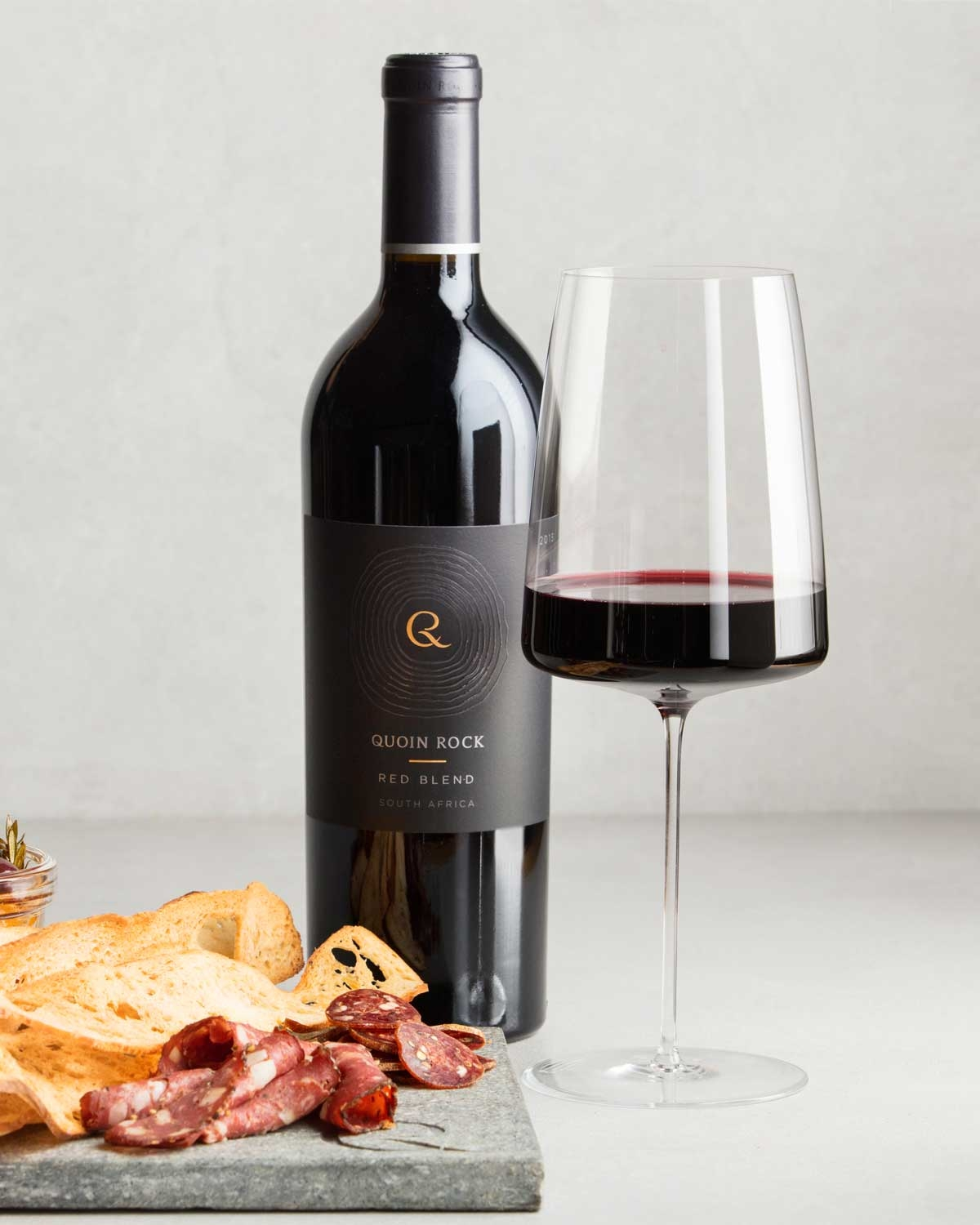 Eine Flasche Quoin Rock Red Blend Wein aus Südafrika mit einem dunklen Etikett mit goldener und weißer Schrift und einem kreisförmigen Design, das sich um den Buchstaben Q dreht.