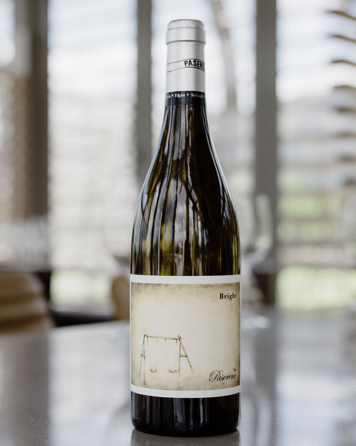 Eine Flasche Weißwein mit einem silbernen Verschluss. Das Etikett zeigt eine sepiafarbene Abbildung einer leeren Schaukel und die Aufschrift Bright by Pasarene.