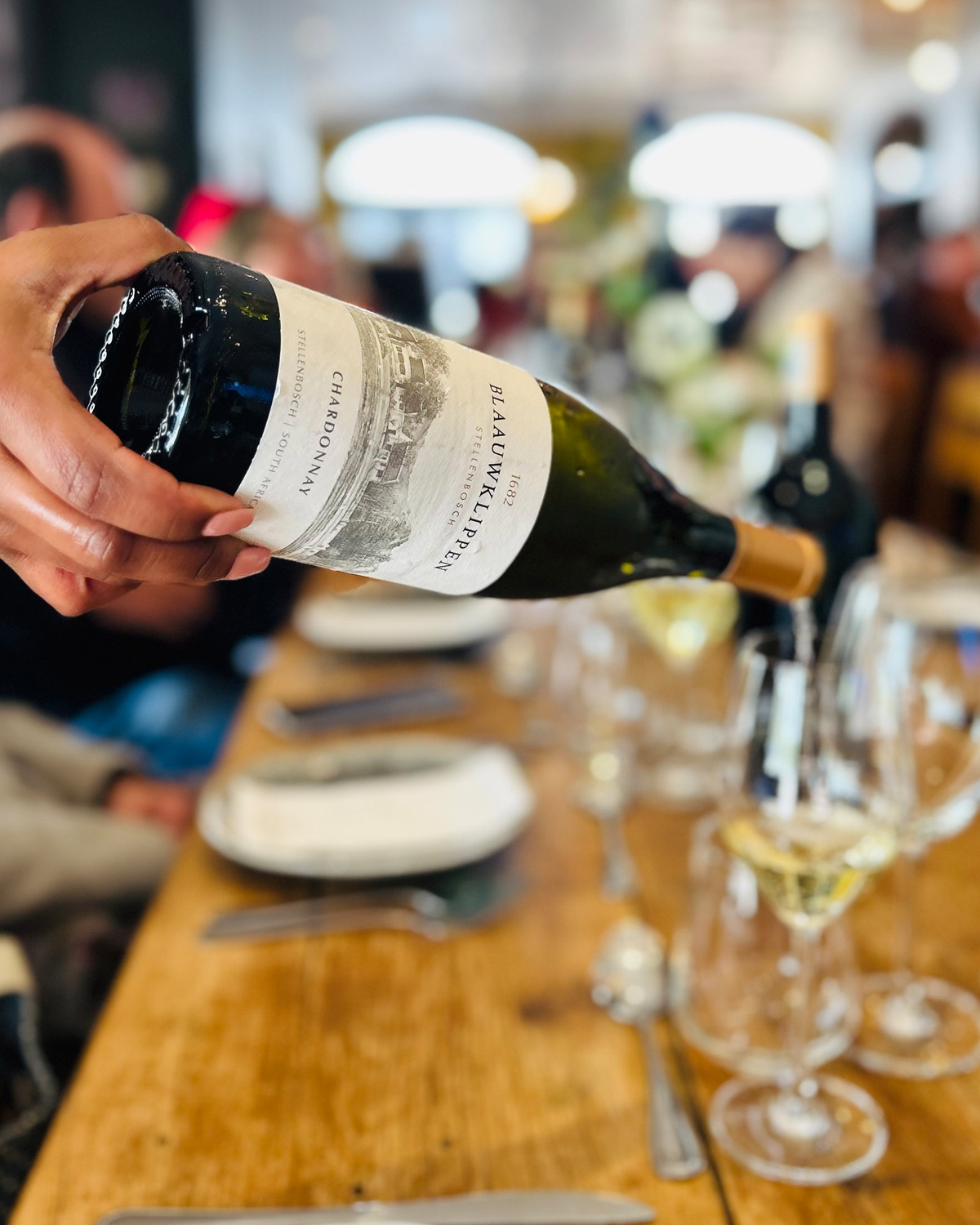 Eine Flasche Blaauwklippen 1682 Chardonnay Wein aus dem Westkap, Südafrika. Auf dem Etikett ist eine Landschaftsskizze mit Gebäuden und Bäumen abgebildet, und die Flasche ist mit einer Goldfolie verschlossen.