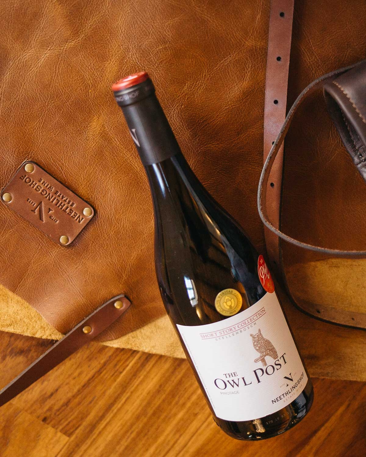 Eine Flasche Neethlingshof Estates The Owl Post Pinotage Wein mit einem schwarzen Verschluss und einem cremefarbenen Etikett mit der Abbildung einer Eule und dem Text Short Story Collection, Stellenbosch.