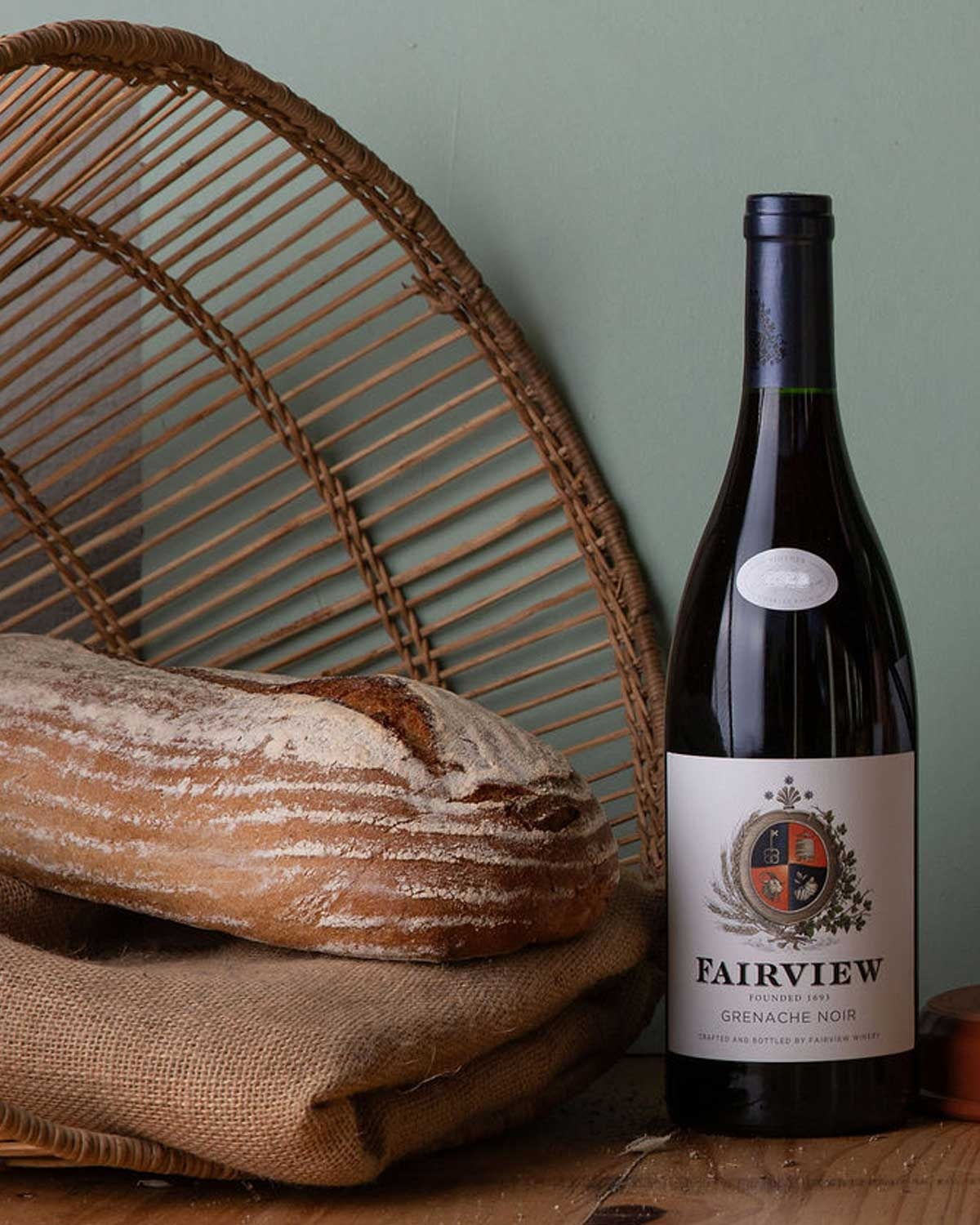 Eine Flasche des Grenache-Weins Fairview Stok by Paaltjie aus Südafrika mit einem cremefarbenen Etikett mit schwarzem und rotem Text und der Abbildung eines Weinbergs mit Holzpfählen und einem Tor.