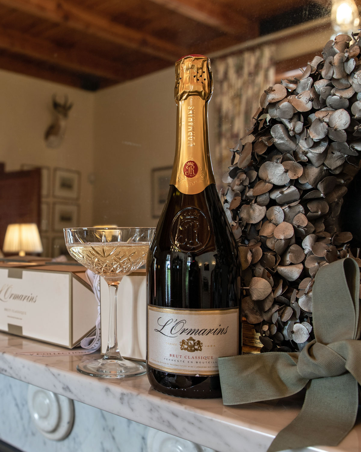 Eine Flasche LOrmarins Brut Classique Sekt mit einem mit Goldfolie umwickelten Hals, geprägtem JR-Logo und einem weißen Etikett mit eleganter goldener und schwarzer Schrift.
