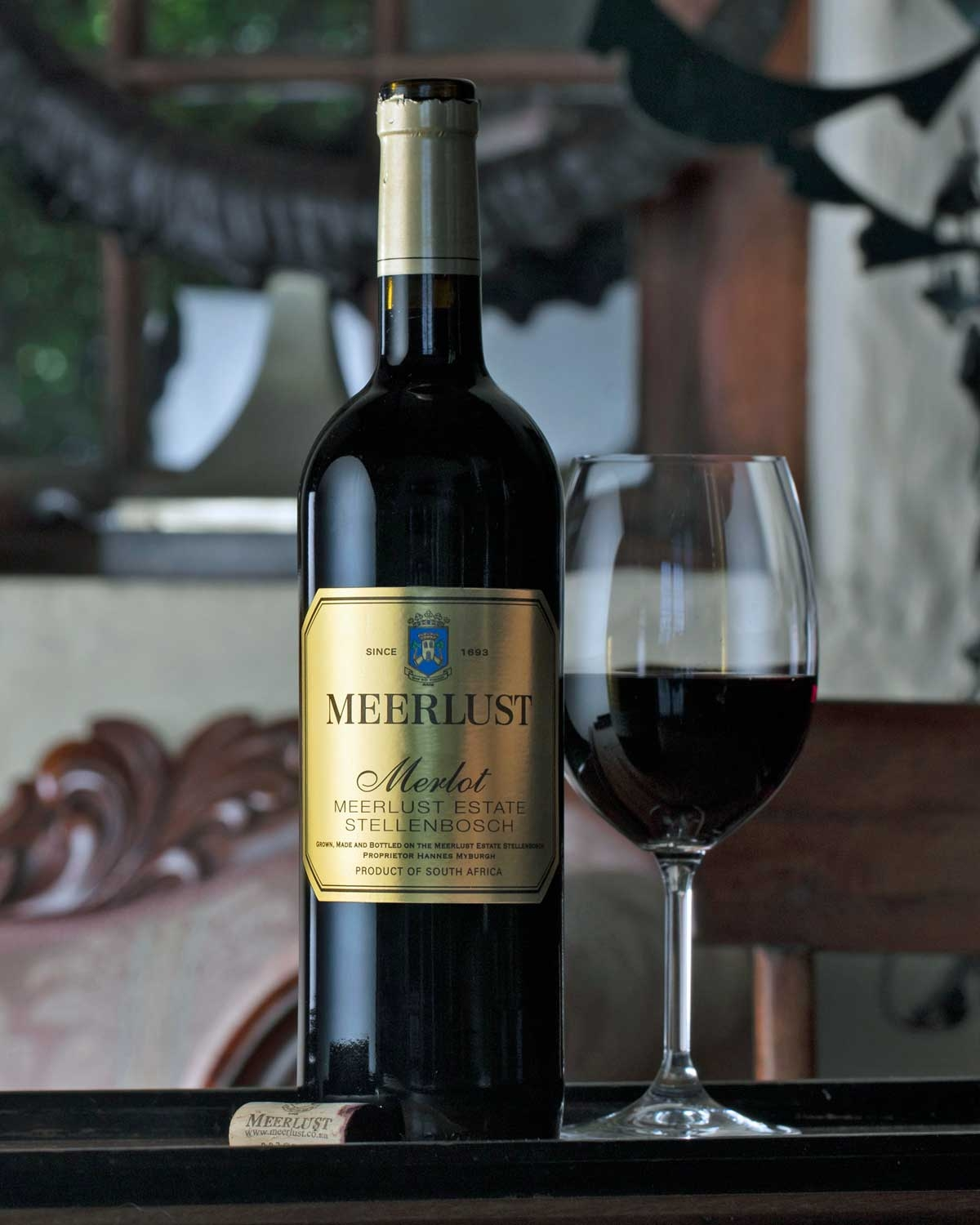 Eine Flasche Meerlust-Merlot-Wein aus Stellenbosch, Südafrika, mit einem Deckel aus Goldfolie und einem goldenen Etikett mit dem Meerlust-Logo und Produktangaben.