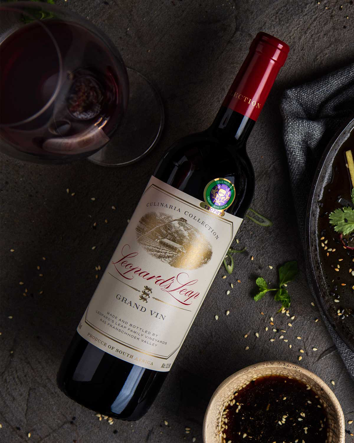 Eine Flasche Leopard's Leap Grand Vin Rotwein aus der Culinaria Collection mit einem cremefarbenen Etikett mit goldenem und rotem Text, einer Abbildung des Weinbergs und roter Folie am Hals. Produkt aus Südafrika.