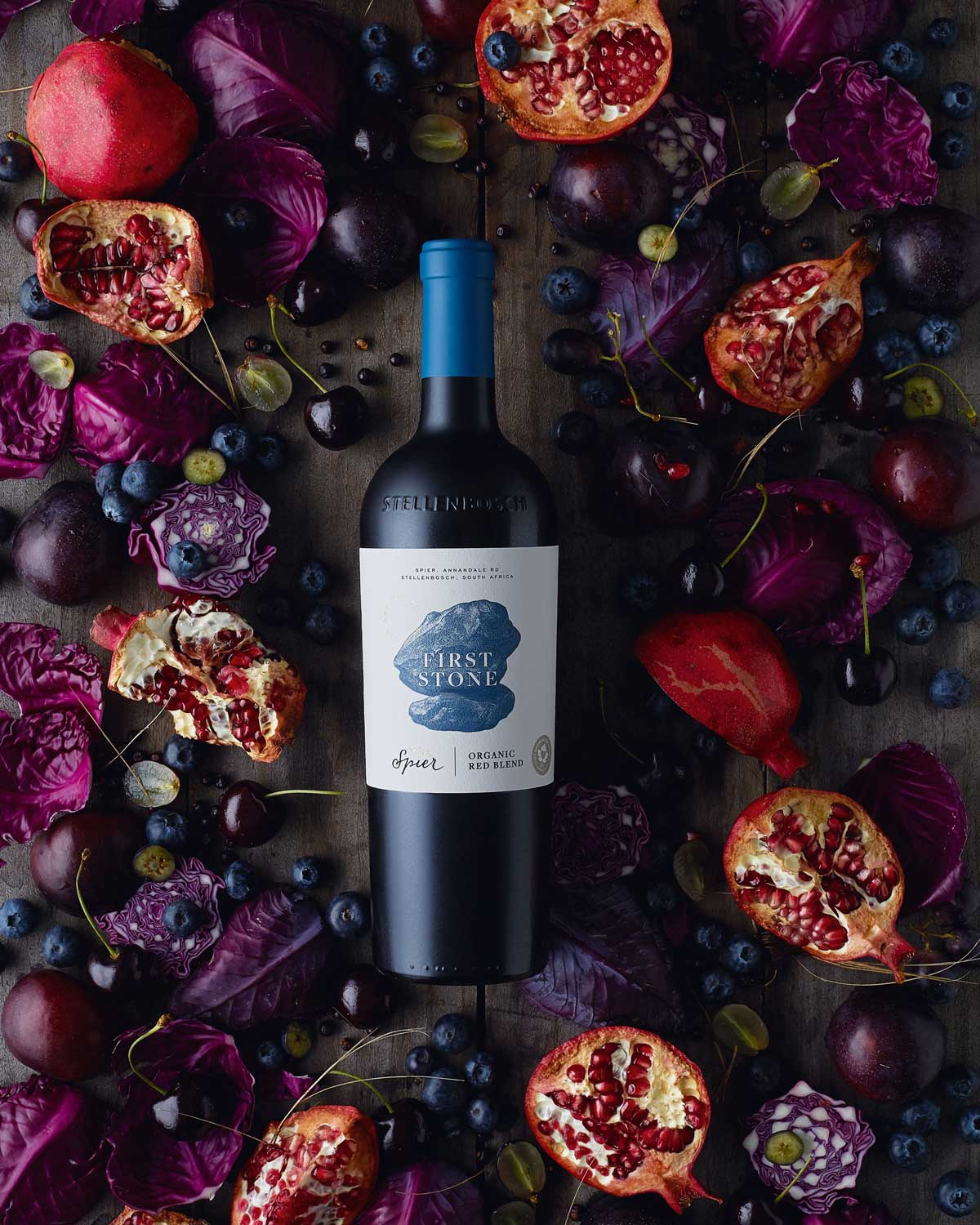 Eine Flasche First Stone Spier Bio-Rotwein mit blauem Etikett und grünem EU-Bio-Zertifizierungslogo mit der Angabe Wein aus Nicht-EU-Landwirtschaft in Deutsch und Englisch.