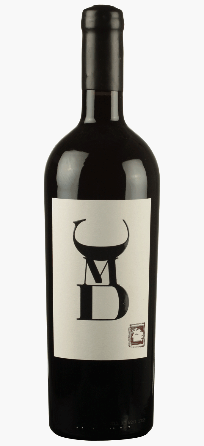 Eine dunkle Weinflasche mit einem weißen Etikett mit fetten schwarzen Buchstaben MD, die von einem Stierhornmuster überlagert werden, steht neben einer passenden schwarzen Schachtel mit demselben Logo.