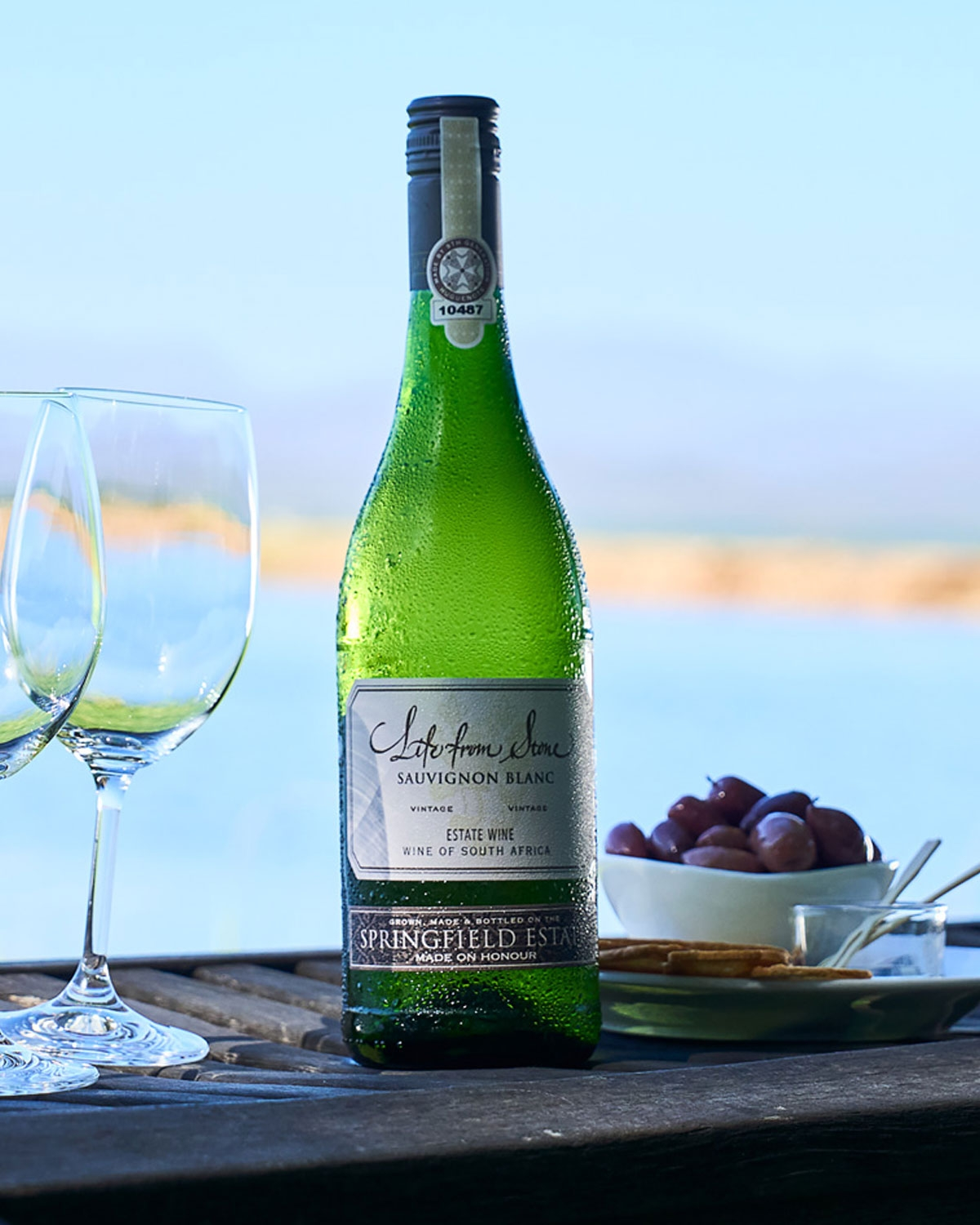 Eine grüne Flasche des Sauvignon Blanc "Life from Stone" von Springfield Estate mit einem weiß-goldenen Etikett, das zeigt, dass es sich um einen Gutswein aus Südafrika handelt. Die Flasche hat ein Goldfoliensiegel und ein detailliertes Emblem auf dem 