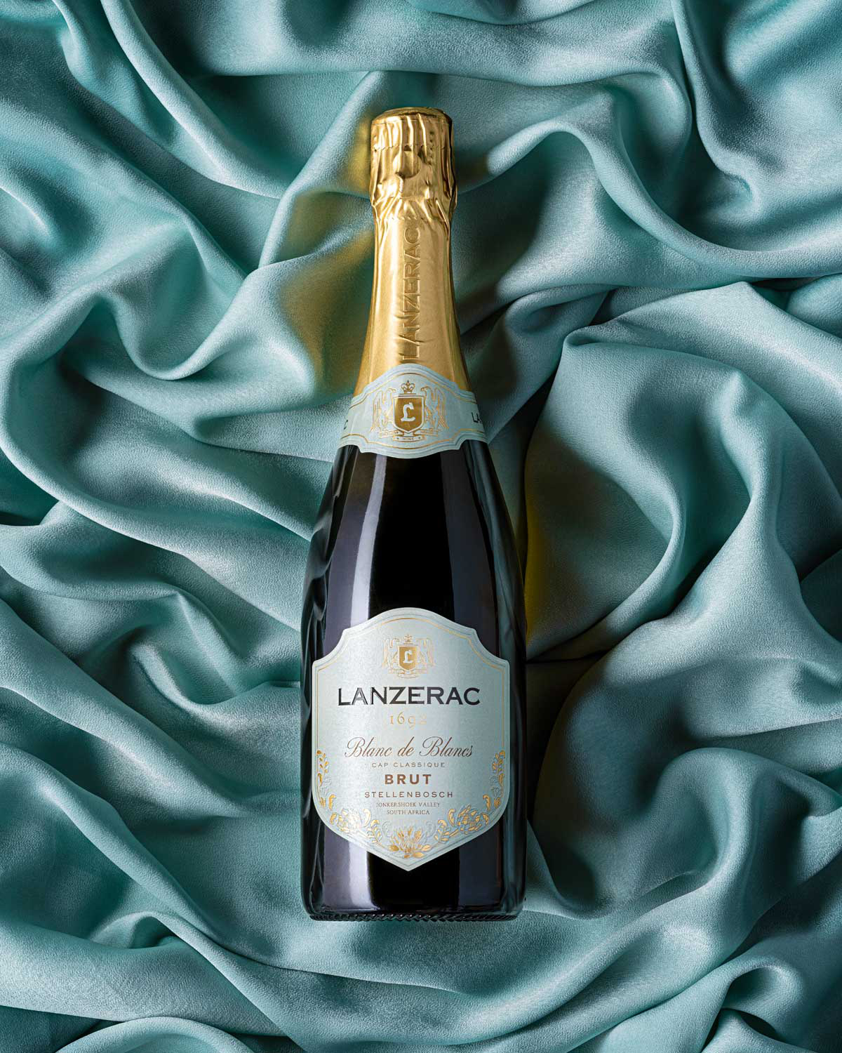 Eine Flasche Lanzerac 1690 Blanc de Blancs Brut Schaumwein mit Goldfolienverschluss und blau-goldenem Etikett, das ein elegantes Branding darstellt.
