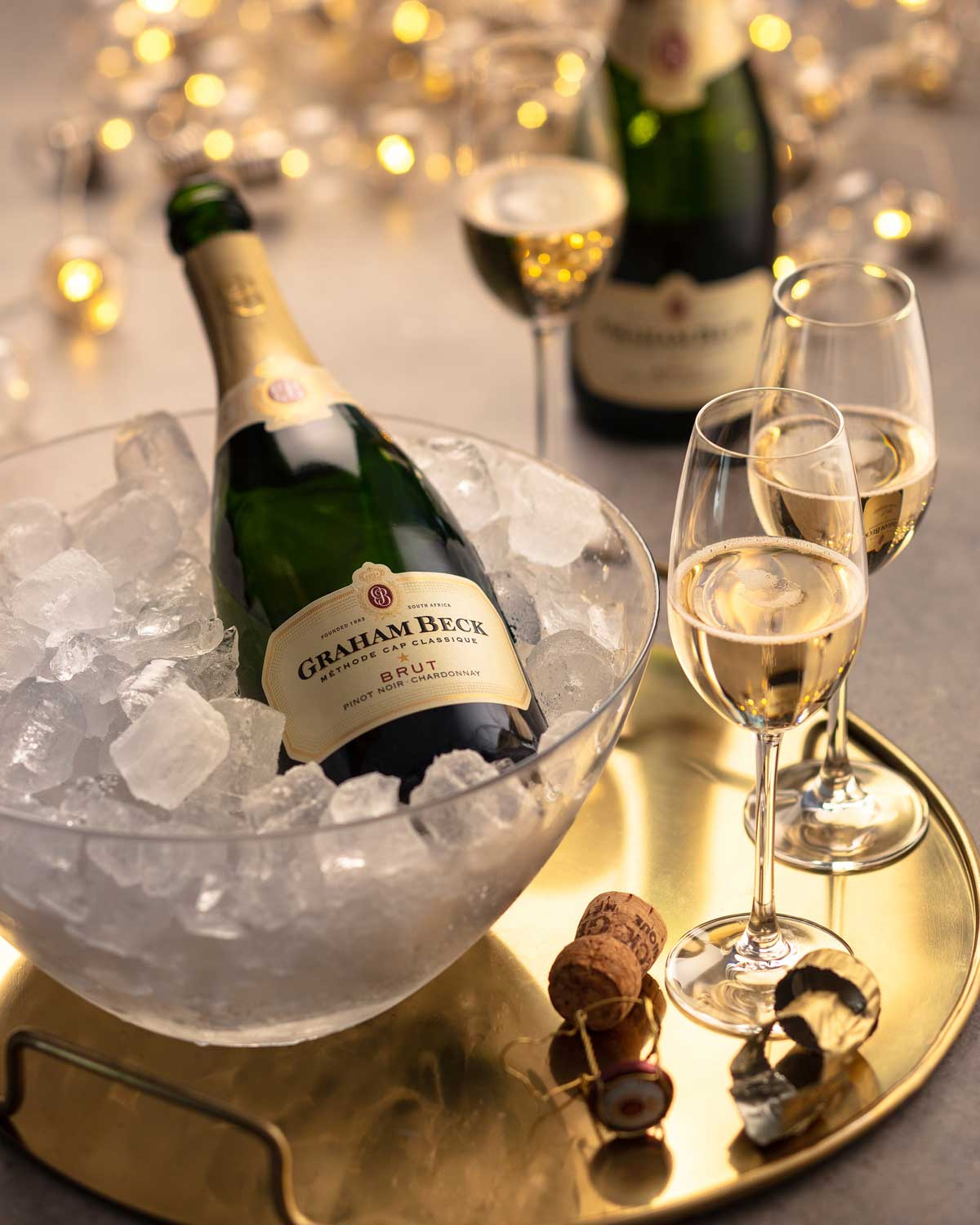 Eine Flasche Graham Beck Brut Schaumwein mit einem Hals aus Goldfolie und einem cremefarbenen Etikett mit roten und goldenen Akzenten. Auf dem Etikett steht, dass es sich um einen südafrikanischen Wein aus Pinot Noir und Chardonnay handelt.