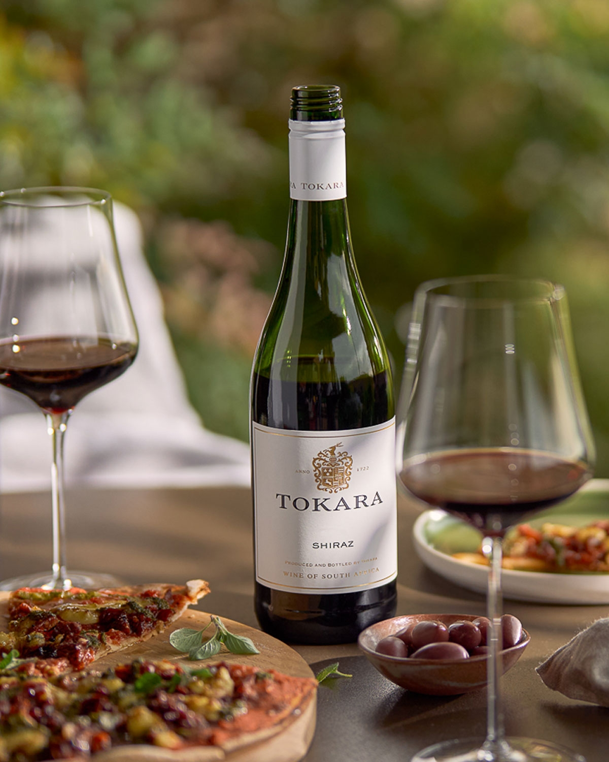 Eine Flasche Tokara Shiraz Wein aus Stellenbosch, Südafrika, mit weißem Etikett mit goldener und schwarzer Schrift, goldenem Emblem und weißem Verschluss.