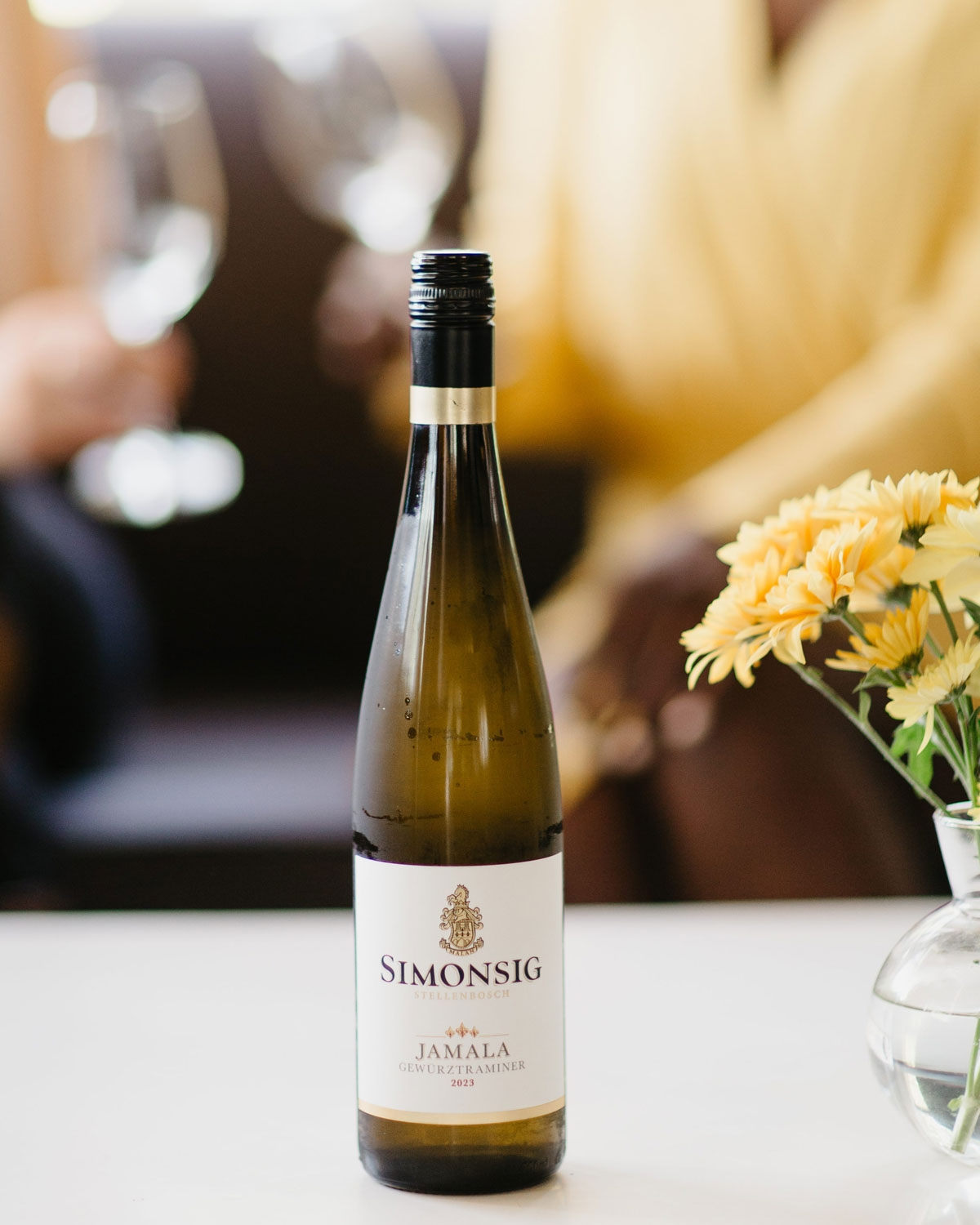 Eine Flasche Simonsig Jamala Gewürztraminer mit goldenem Verschluss, weißem Etikett und schwarz-goldenem Text, der ein Wappen über dem Markennamen zeigt. Die Flasche ist vor einem schlichten, hellen Hintergrund fotografiert.