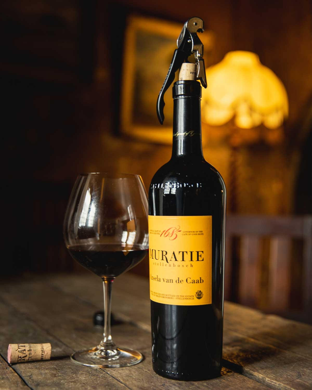 Eine Flasche Muratie Stellenbosch Rotwein mit der Aufschrift Ansela van de Caab, goldgelbem Etikett und schwarzer Schrift, mit Unterschrift und Korkverschluss.